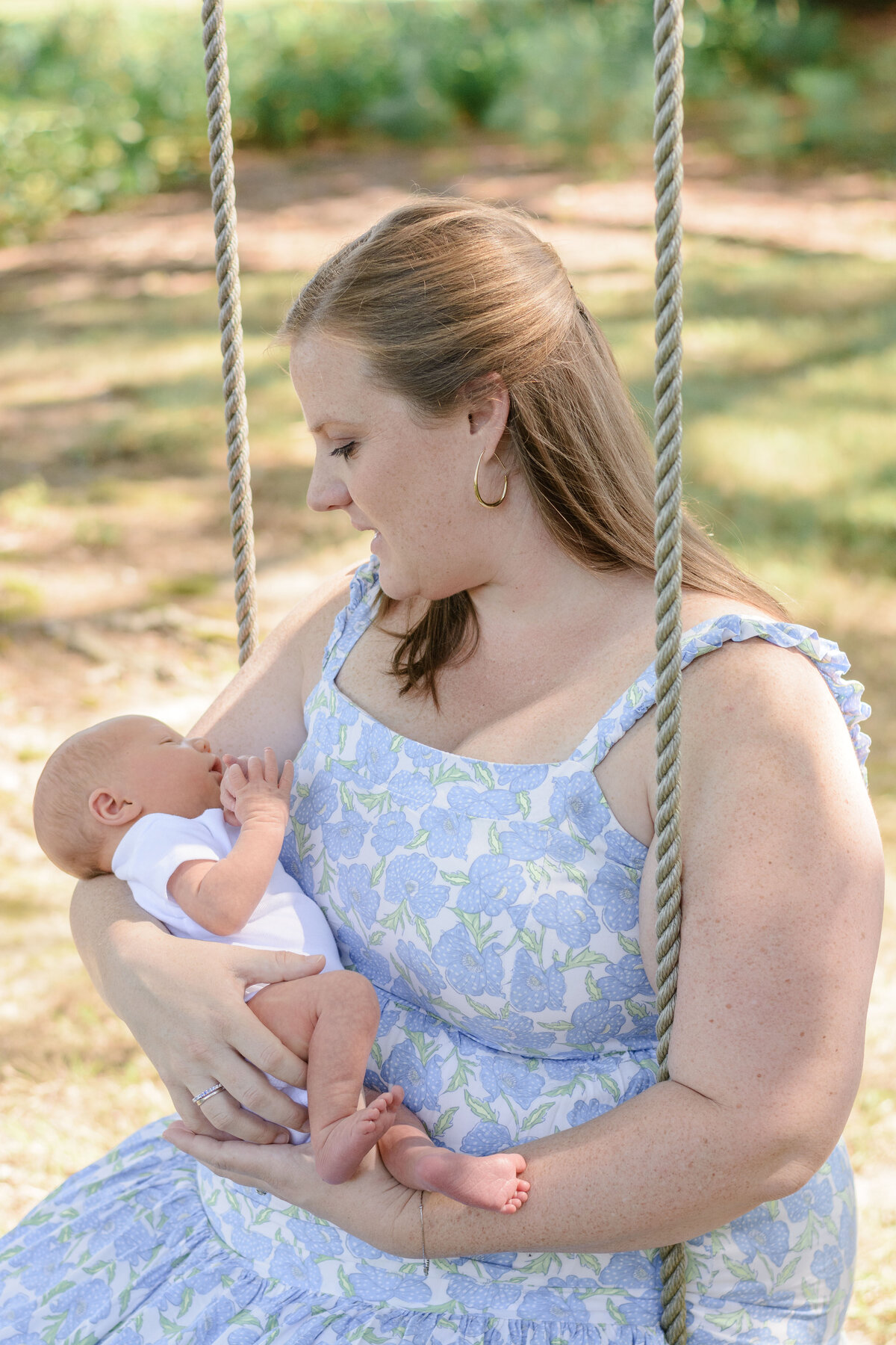 Mother holding her newborn on a swing under a tree