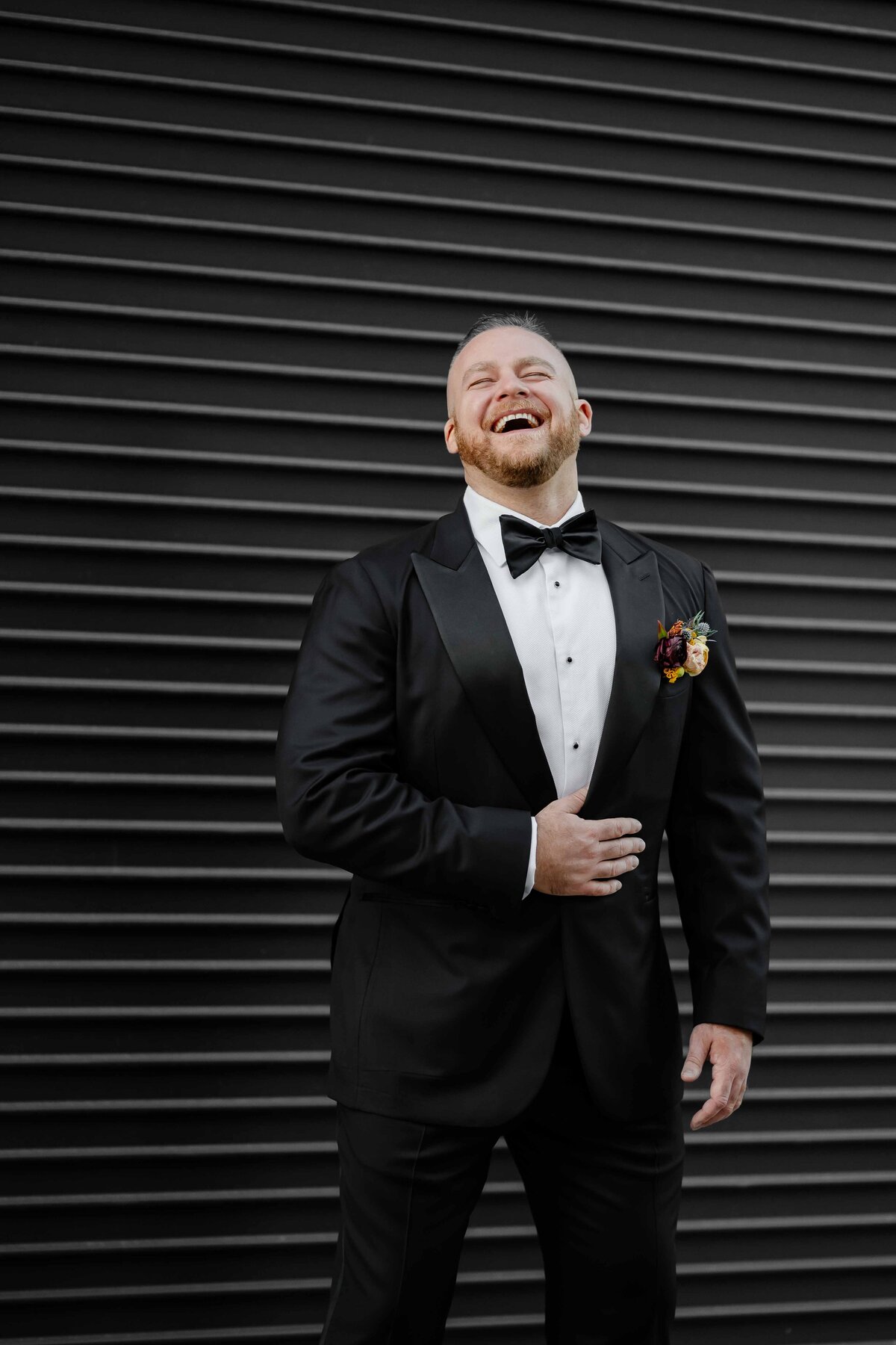 Groom laughs in front of a black wall