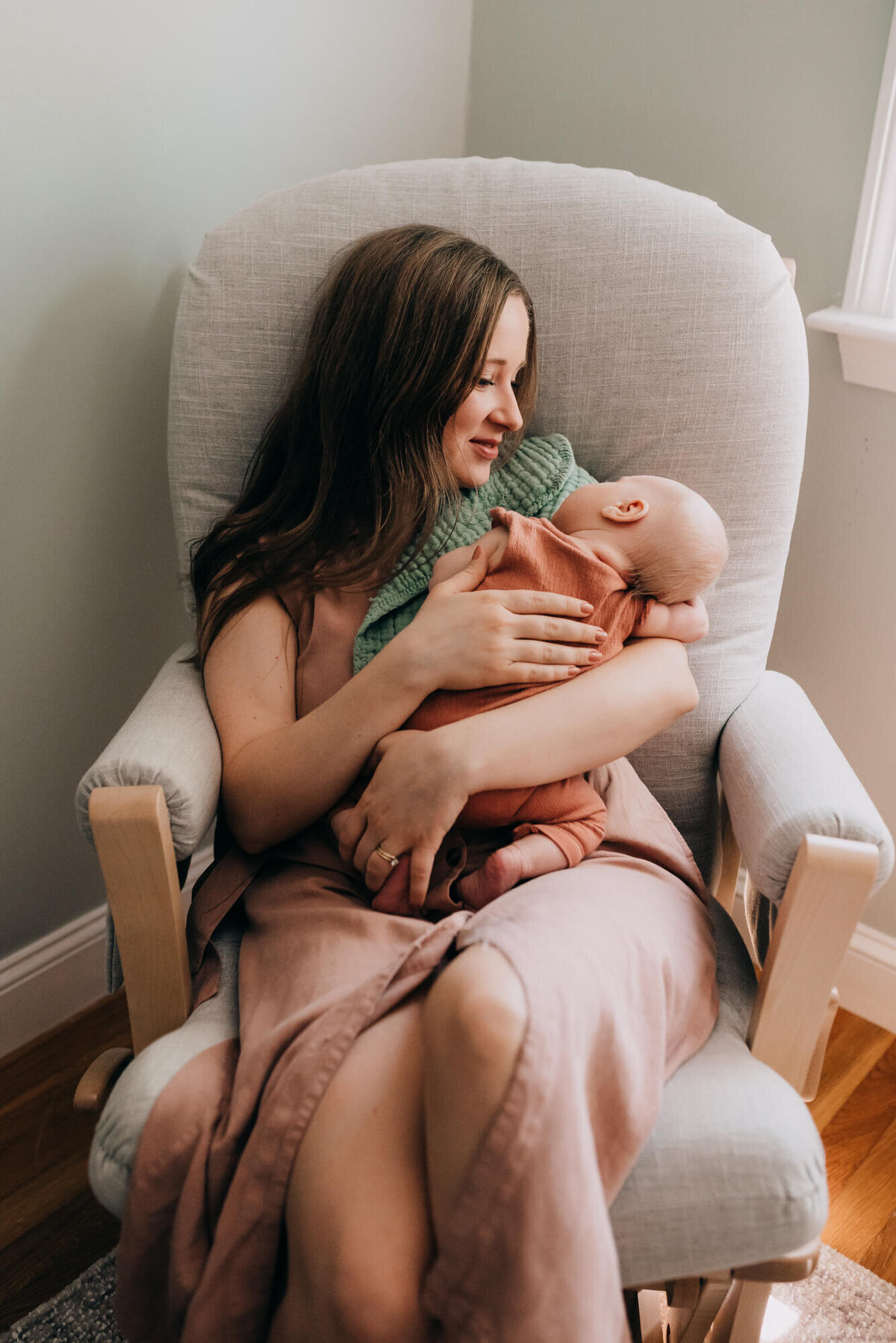 A young mother holds her newborn daughter while sitting in a rocker during her photoshoot with Boston Newborn Photographer, Allison Wolf