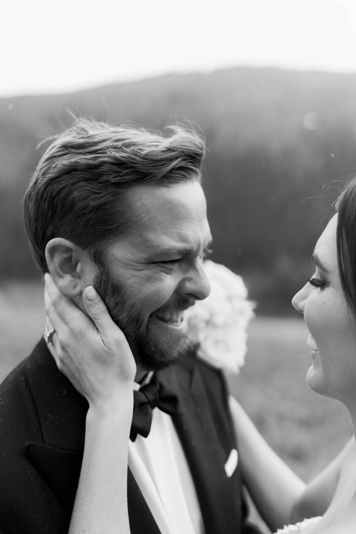 Black and white photo of a smiling groom with a mountain backdrop