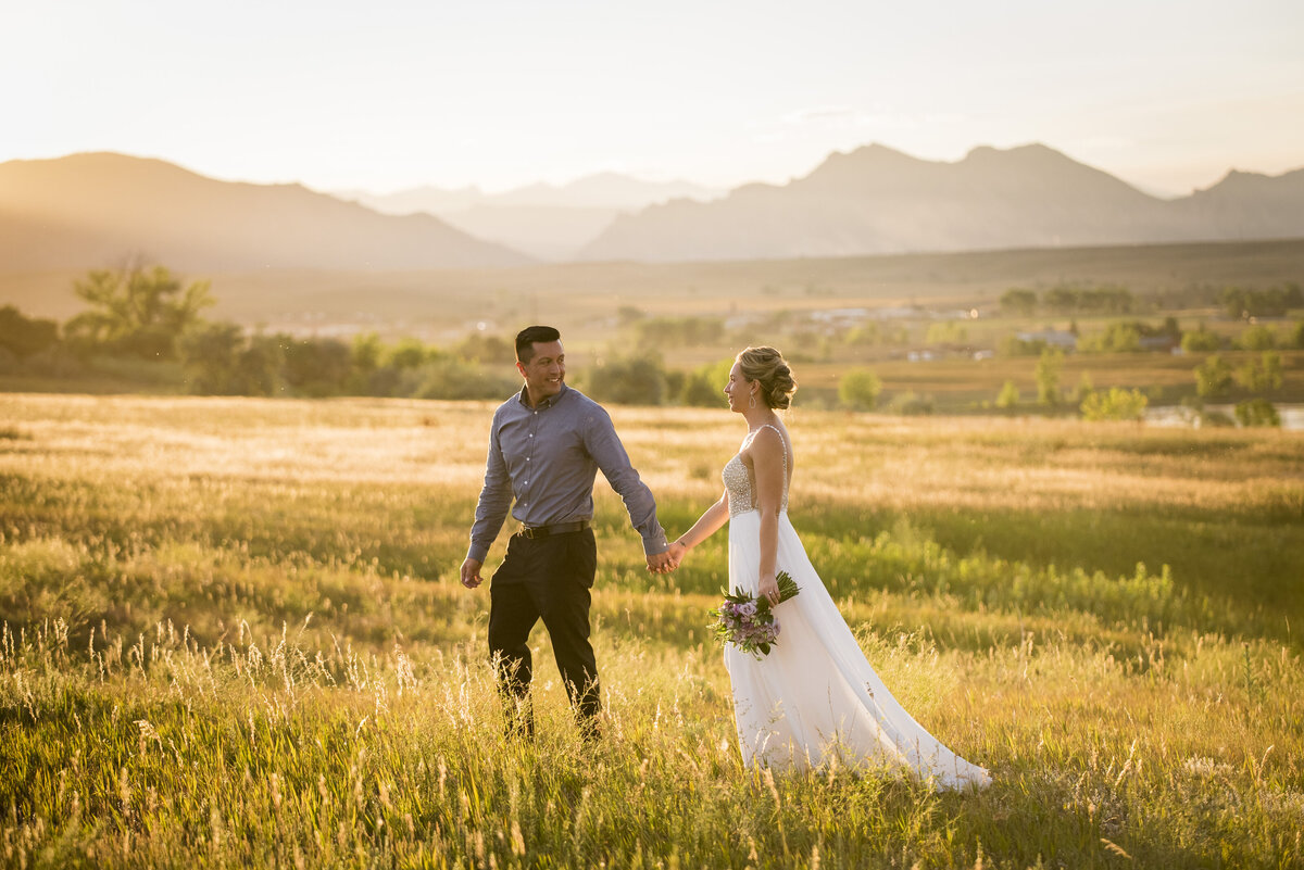 A groom leads his bride through a field at golden hour.