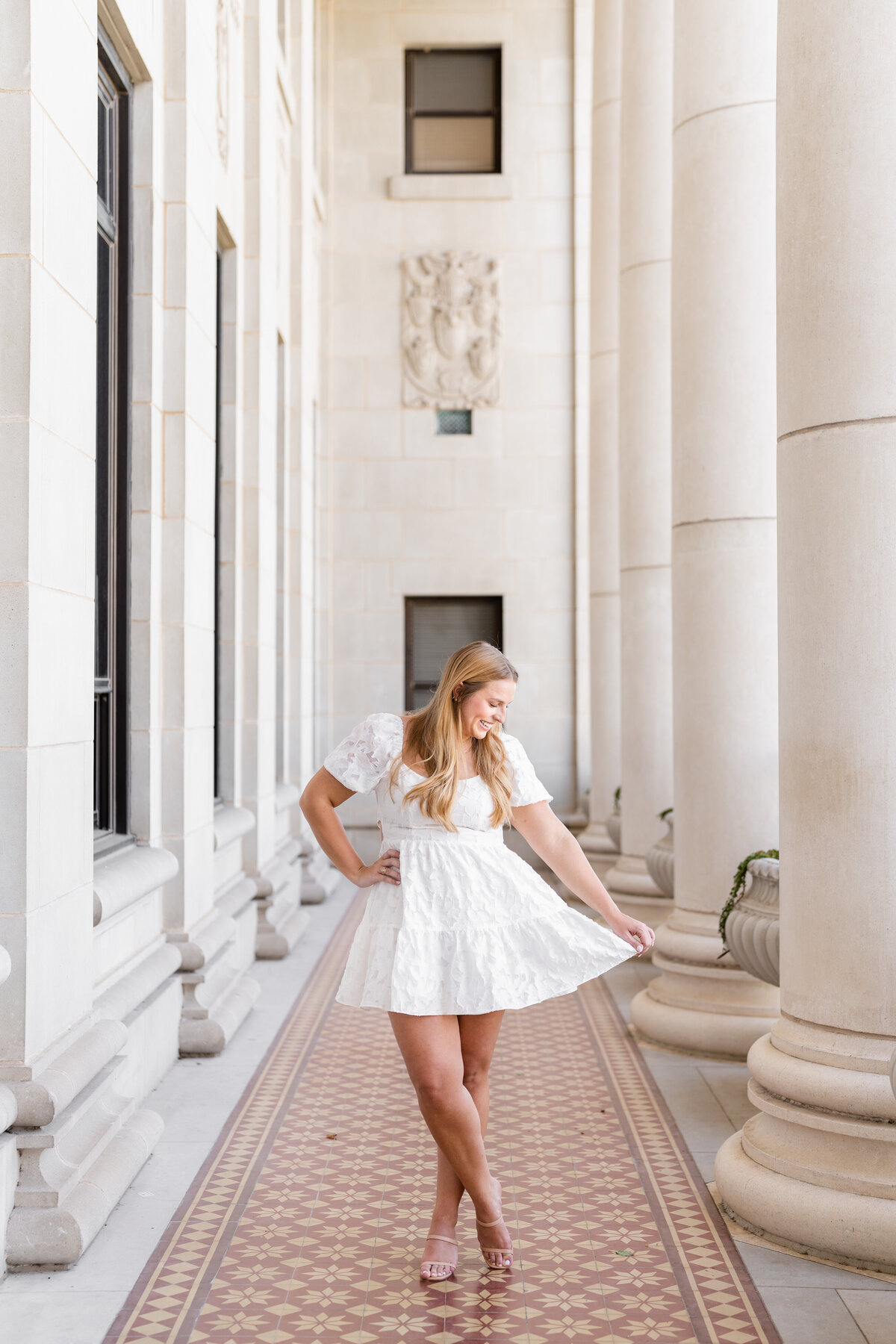 Texas A&M senior girl wearing white dress and holding end while smiling down in the columns of Administration Building