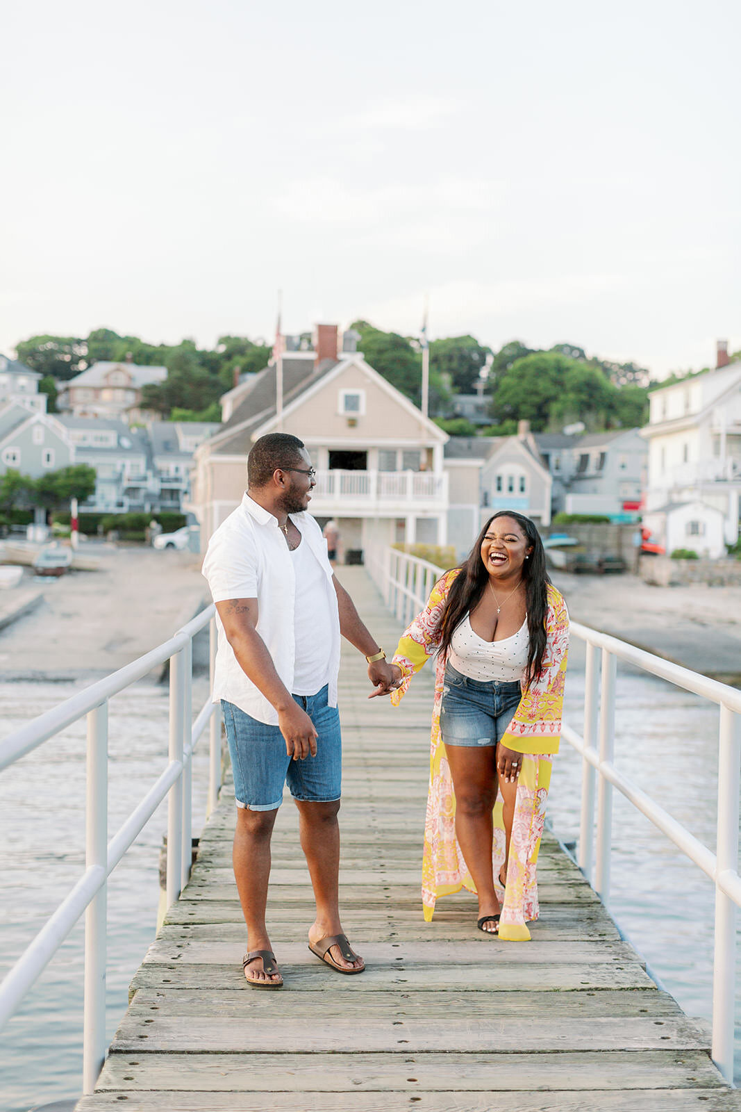 Couple smiling and walking along a pier as they hold hands.