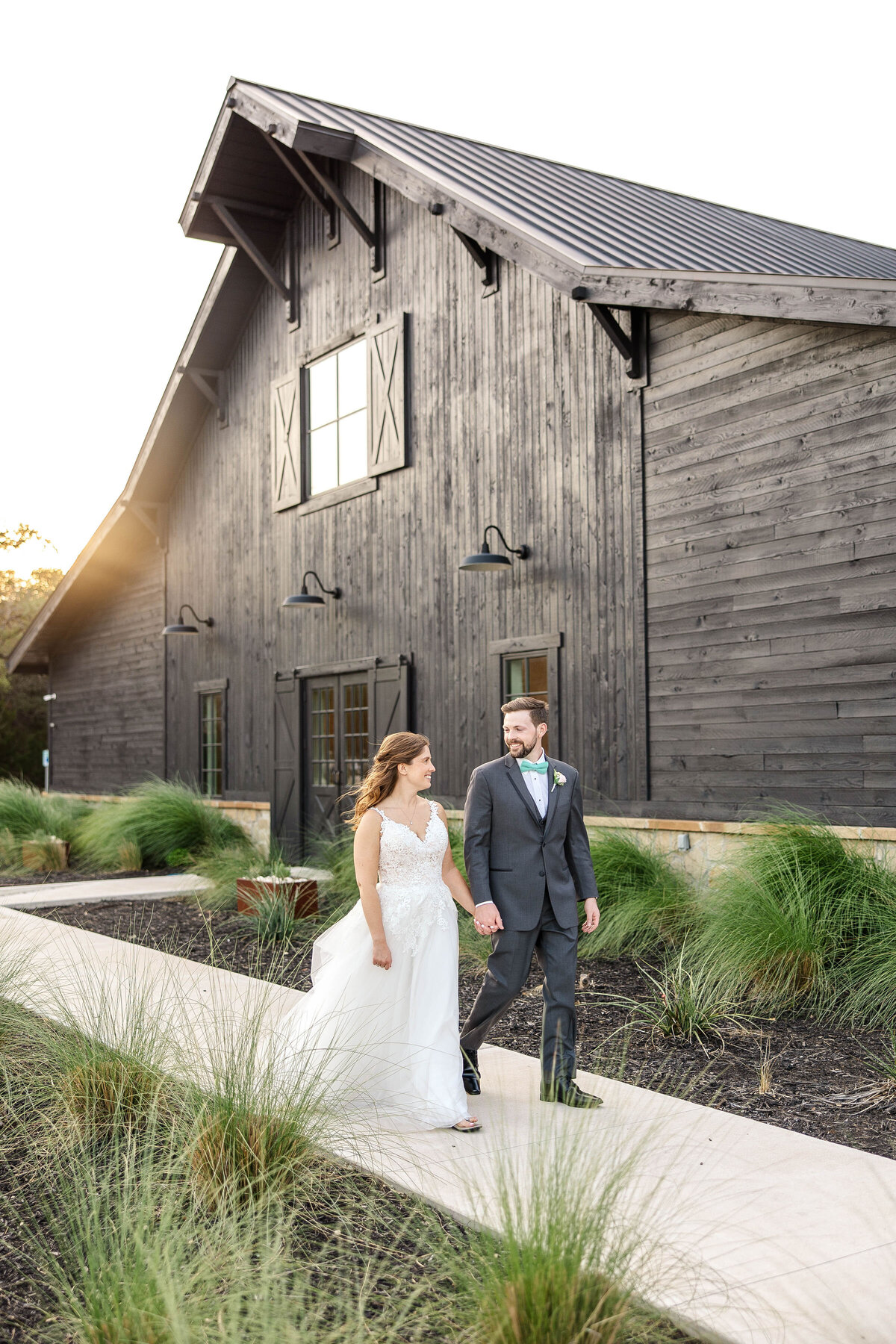 bride and groom hold hands and walk from Morgan Creek Barn  with sunset in Dripping Springs Texas