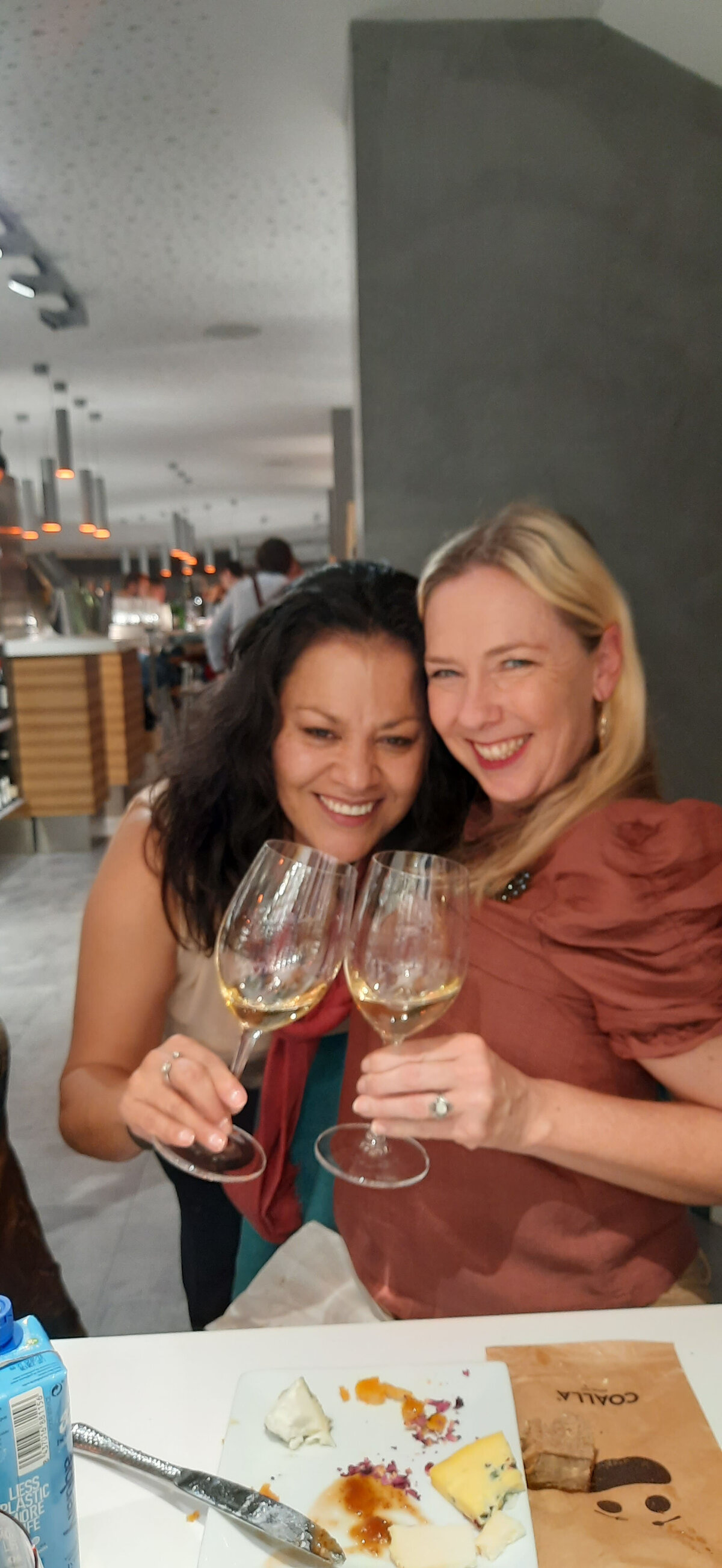 Maria and her friend holding a glass of white wine, with cheese on the table in front of them at Coalla wine bar.