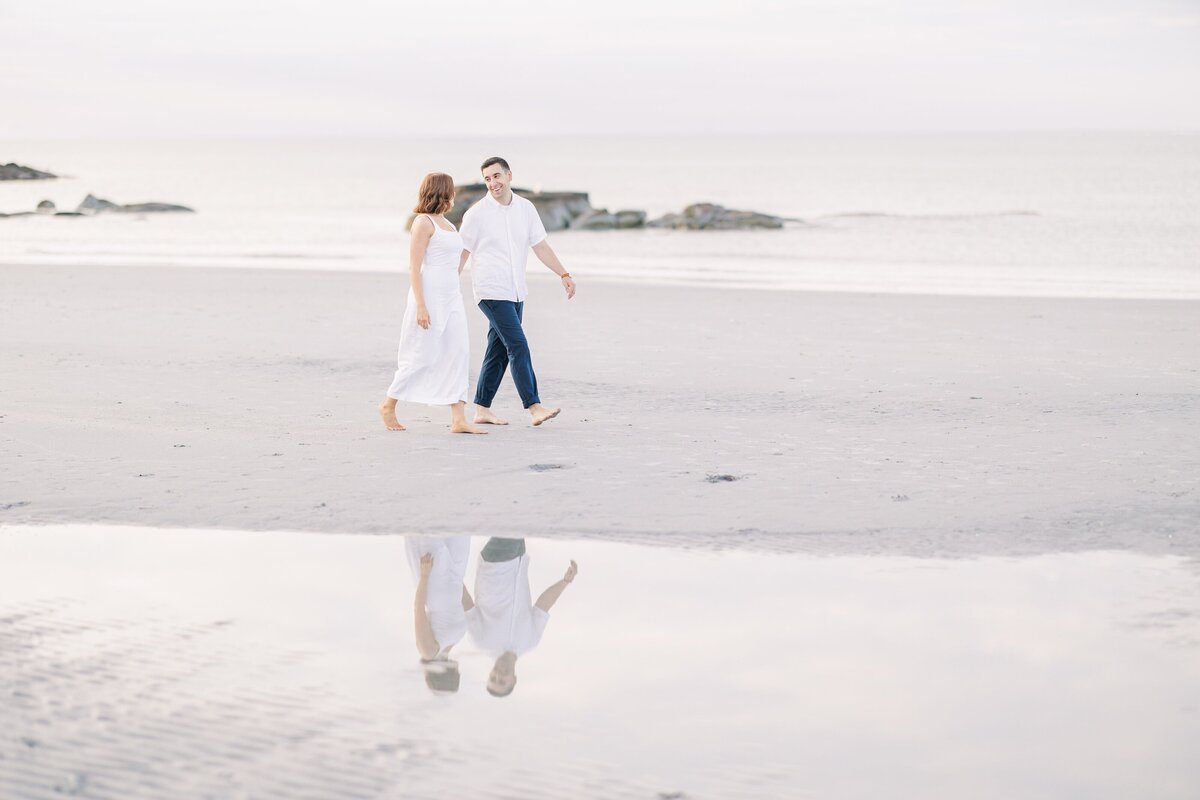 A couple holding hands and walking down Wingaersheek Beach representing a Gloucester engagement photographer's portfolio.