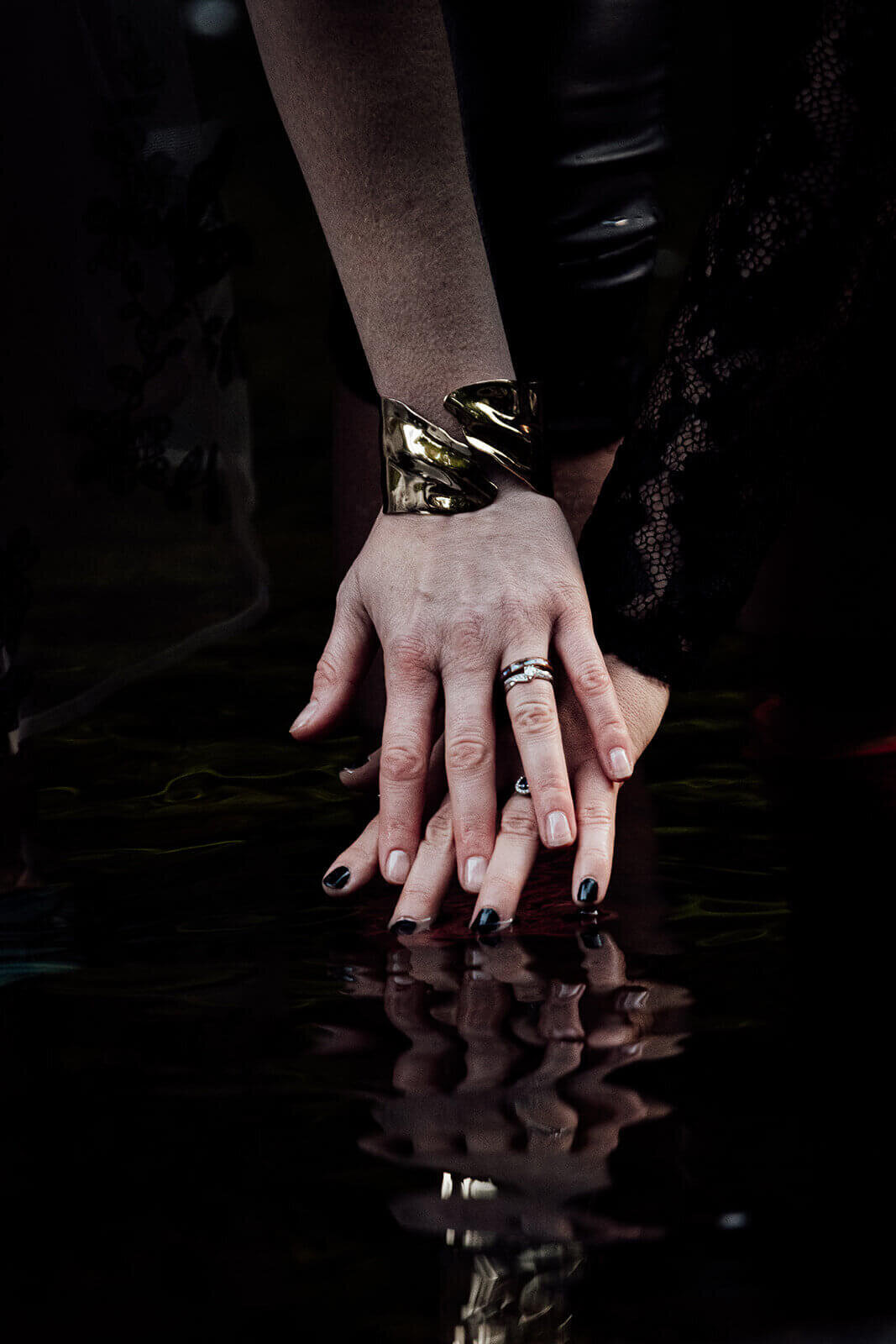 Two brides start to lock fingers above a Perth river with their fingers touching the water.