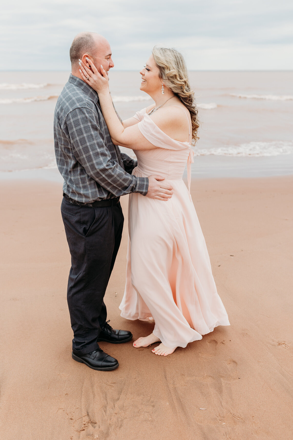 A married couple poses on the shore of Lake Superior for a Duluth wedding photographer, S Jacobson Photography, as the waves crash into the shore.