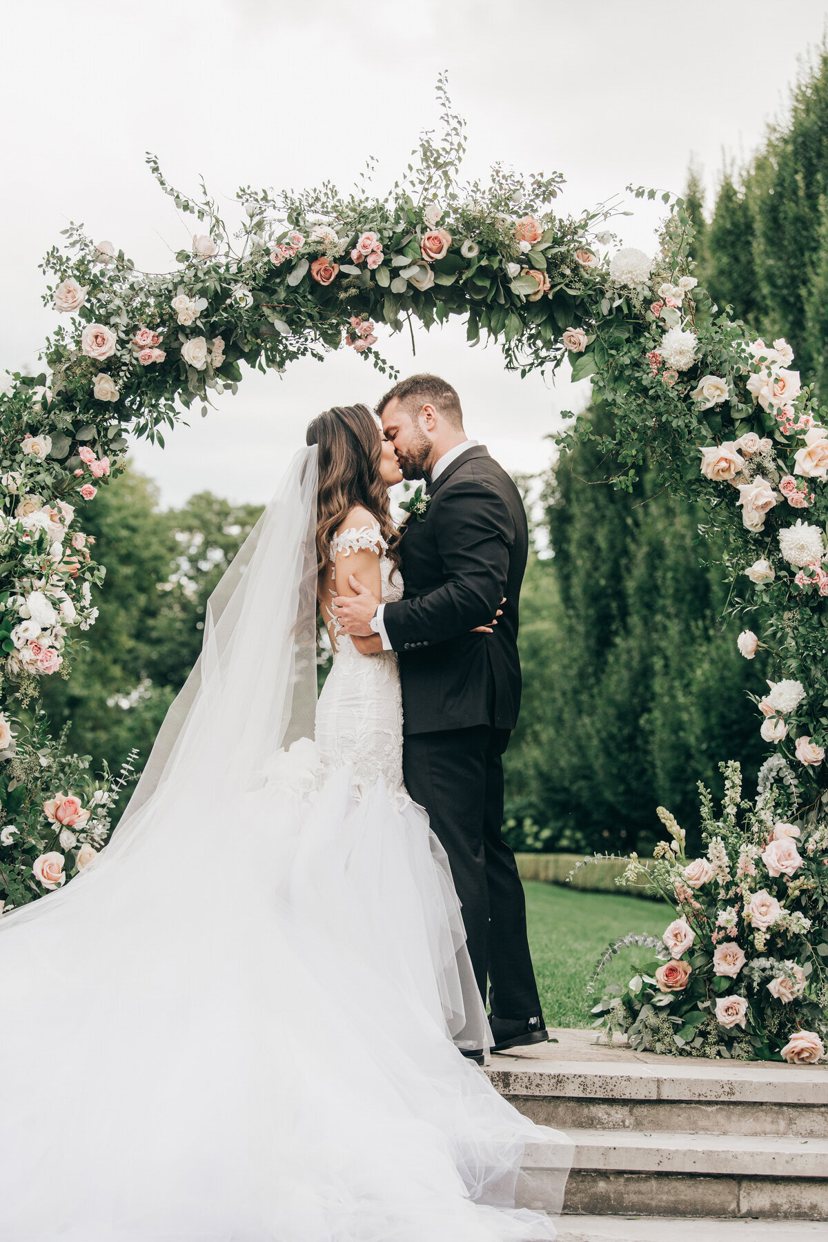 Bride and groom first kiss under luxurious rose arch