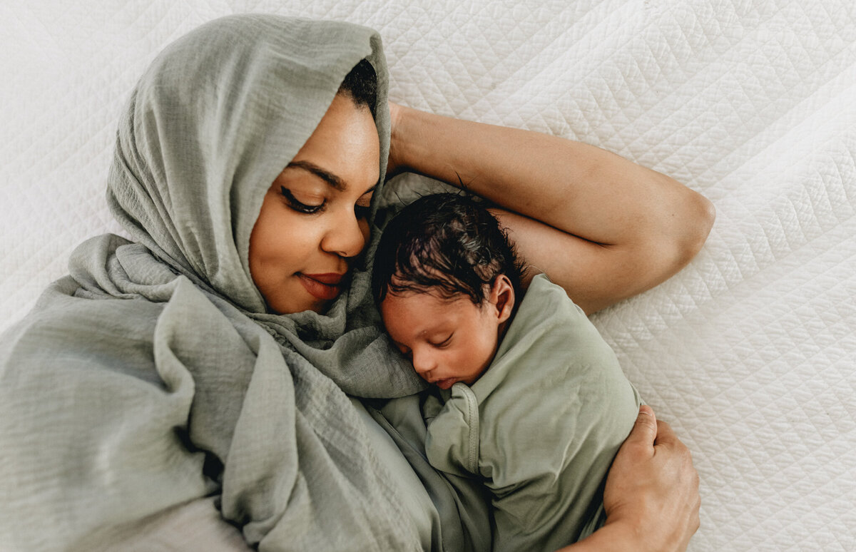 Newborn photography of mother holding newborn babe in bed.