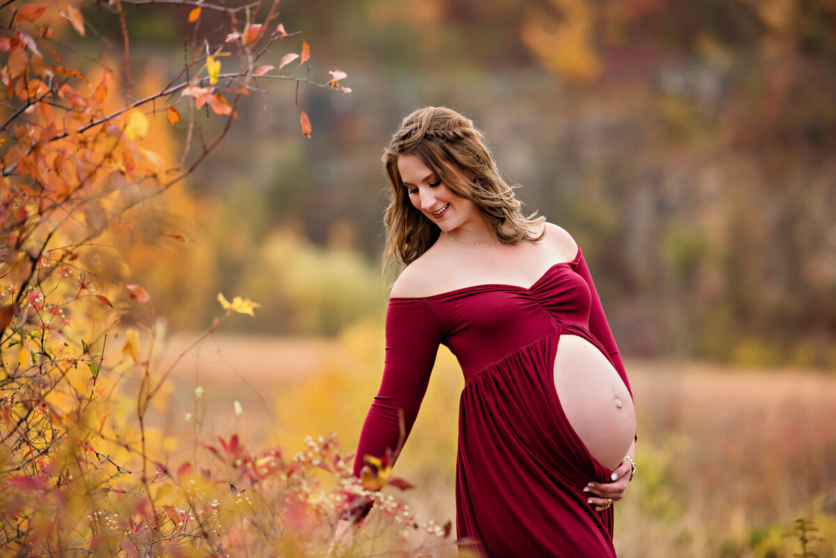 Pregnant woman wearing a red maternity dress with the belly exposed for her fall outdoor maternity photography session