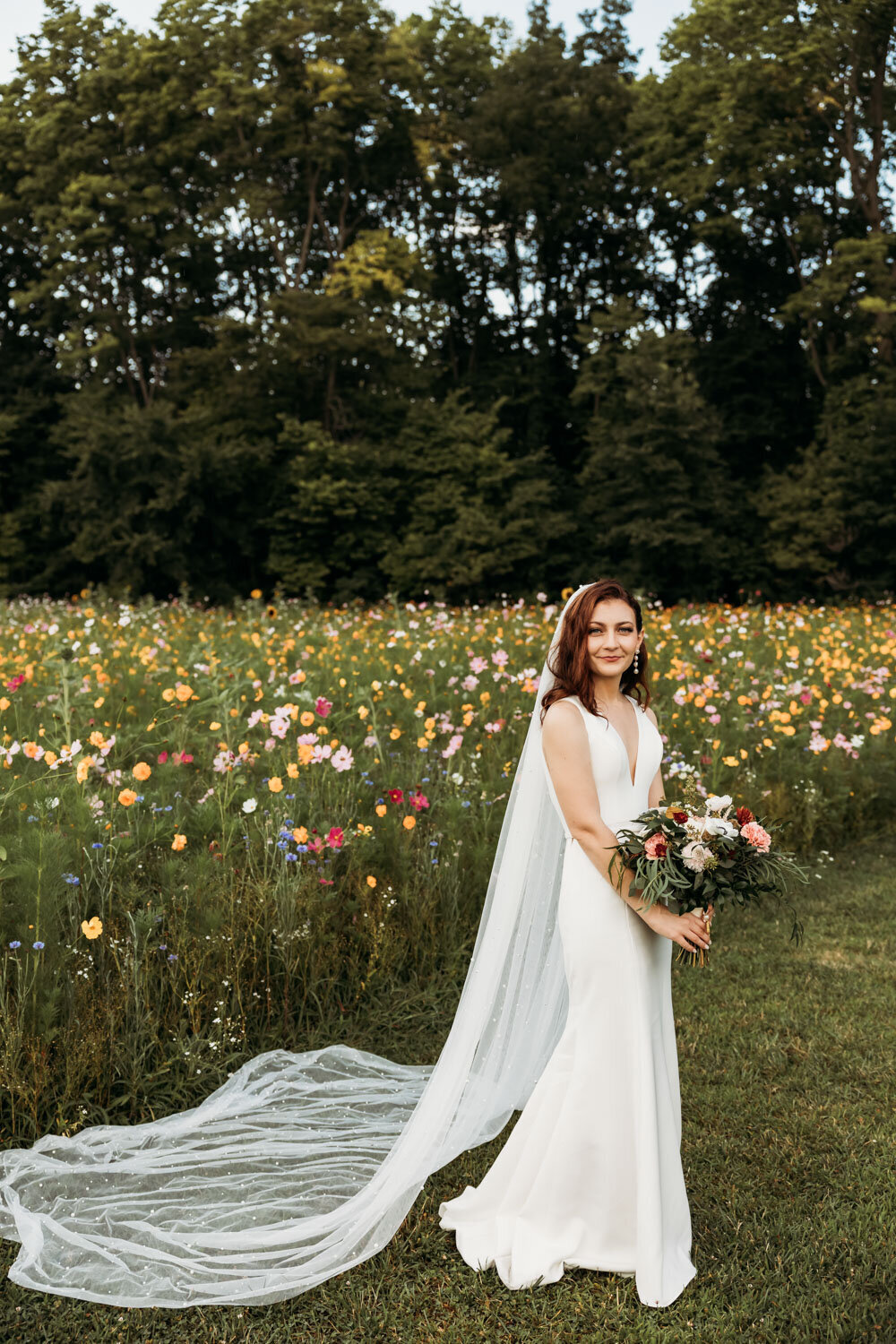 Bride in white gown holding bouquet in wildflower field