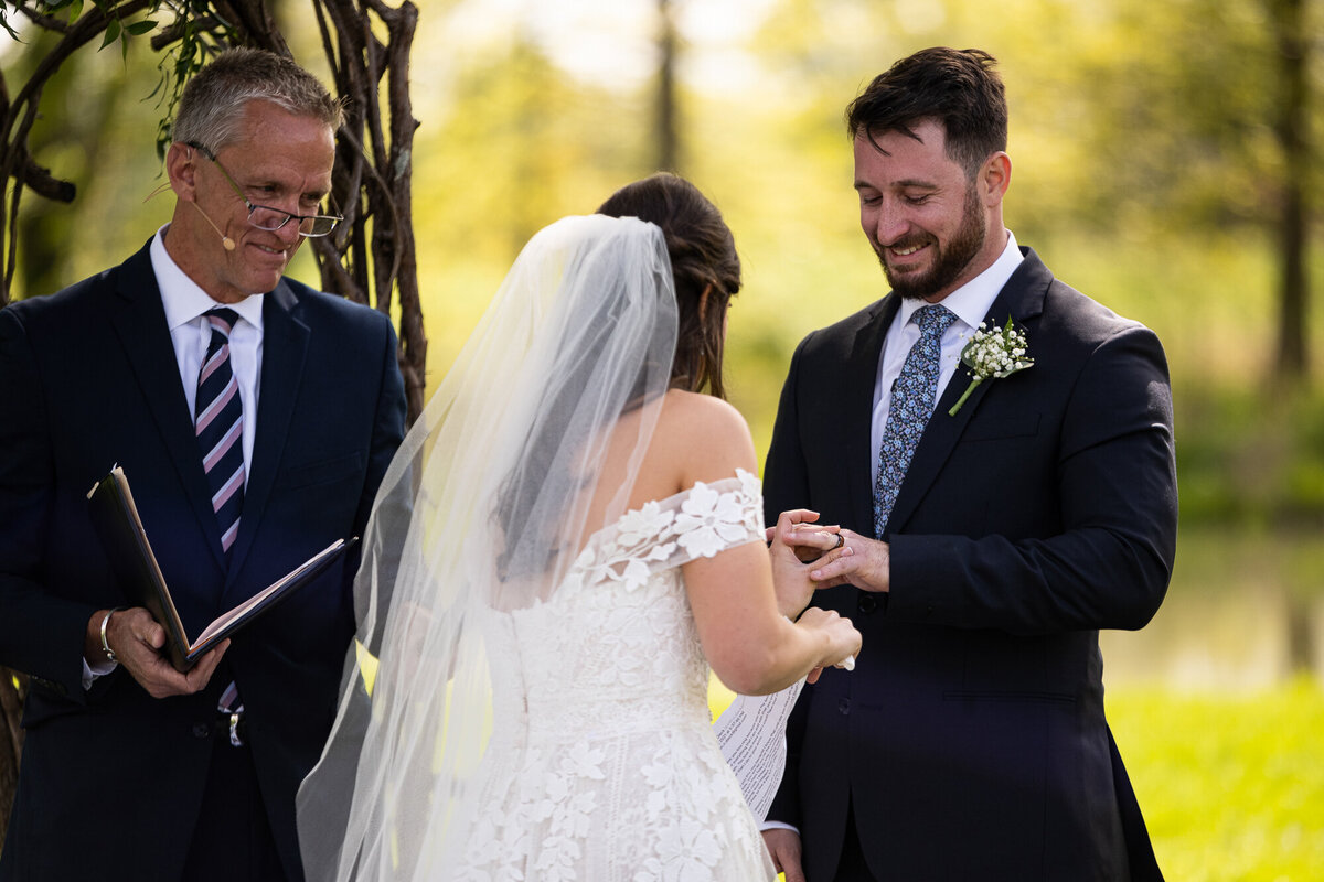Bride slips groom's wedding band on during ceremony at Oak Grove