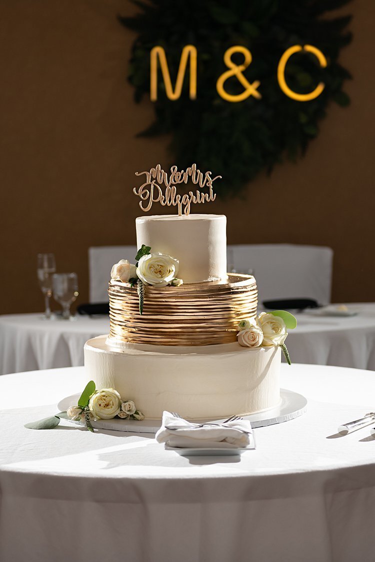 Gold and off-white wedding cake with Mr and Mrs topper and monogram neon sign in background