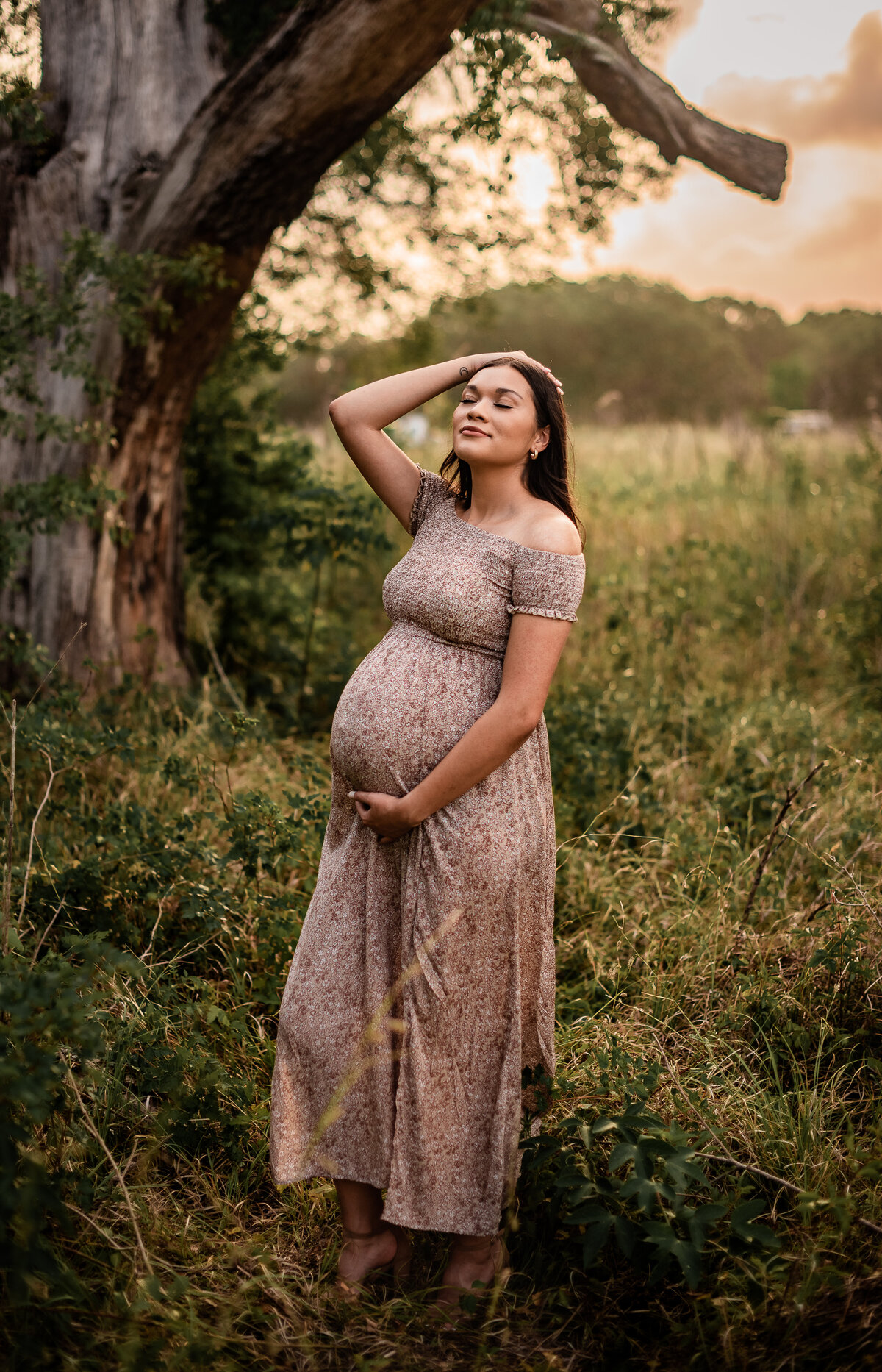A pregnant woman holds her belly bump and looks toward the sky with her eyes closed.