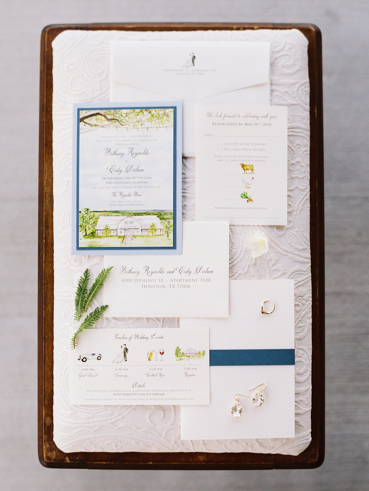Flatlay of wedding stationery suite and earrings and wedding rings