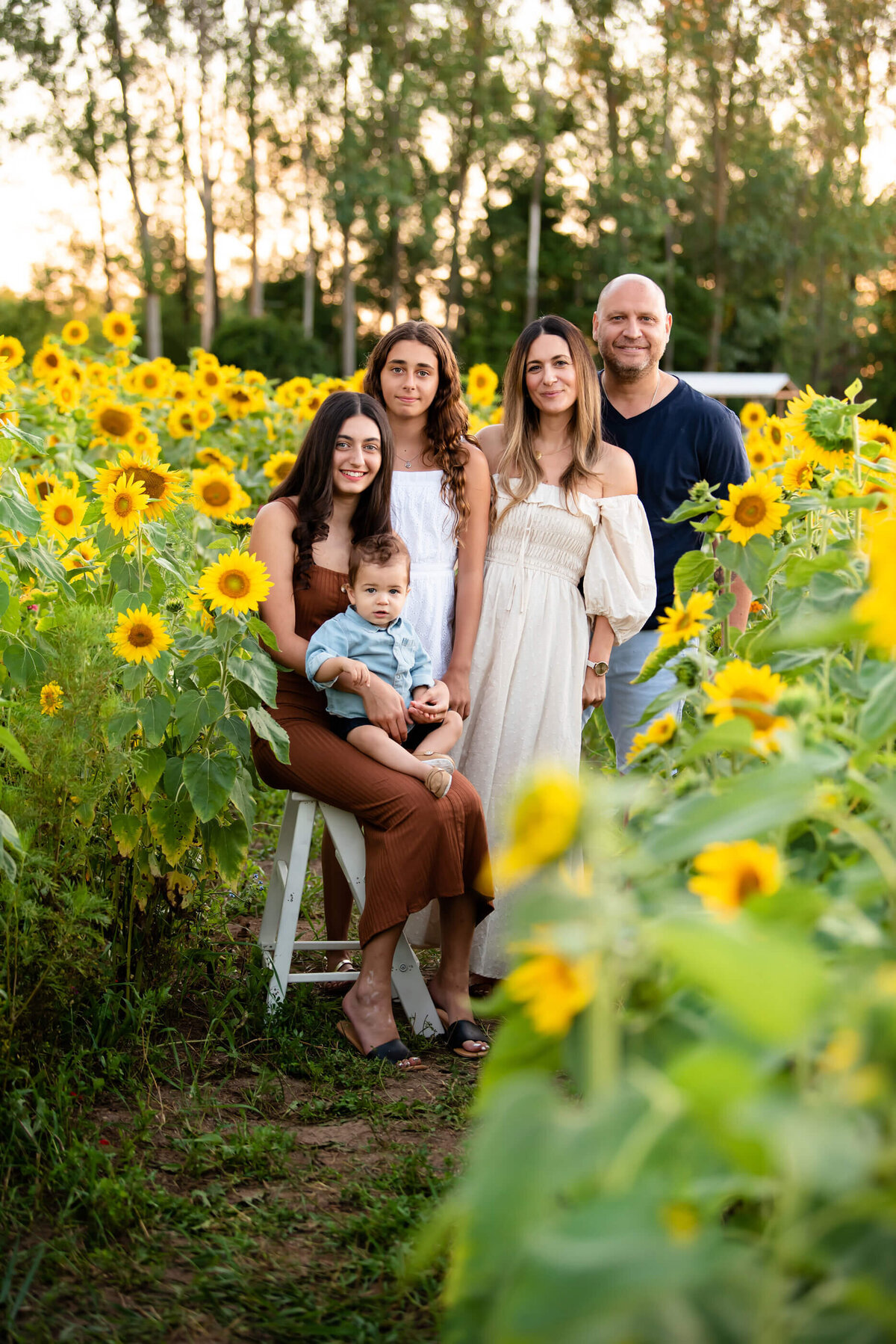 Family of five, mom and dad, two teenage daughters and baby boy standing in a sunflower field for their family photos in Burlington, On