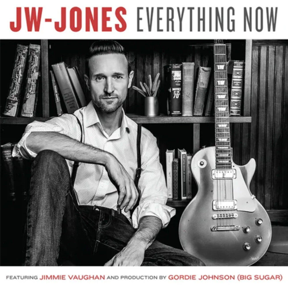 Guitarist album cover JW Jones Everything Now sitting in front of book shelf with guitar standing up beside him in black and white