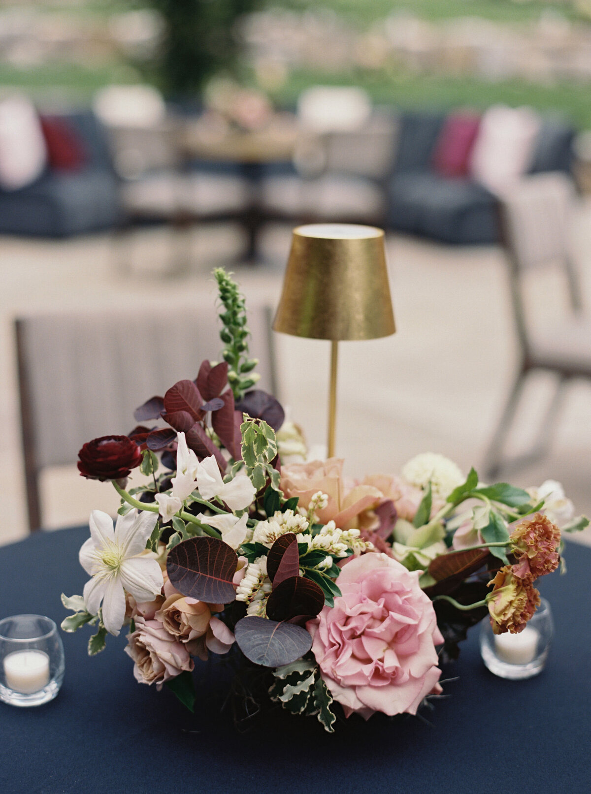 Moody welcome party for fall wedding weekend. Tented reception for outdoor wedding reception at Blackberry Farm. Moody floral design with colors of deep magenta, mauve, eggplant, blush, and natural greens. Rich tones with roses, mums, and smokebush foliage. Romantic candle light and large trees create a magical setting for a welcome party. Destination wedding at Blackberry Farm. Design by Rosemary & Finch Floral Design in Nashville, TN.