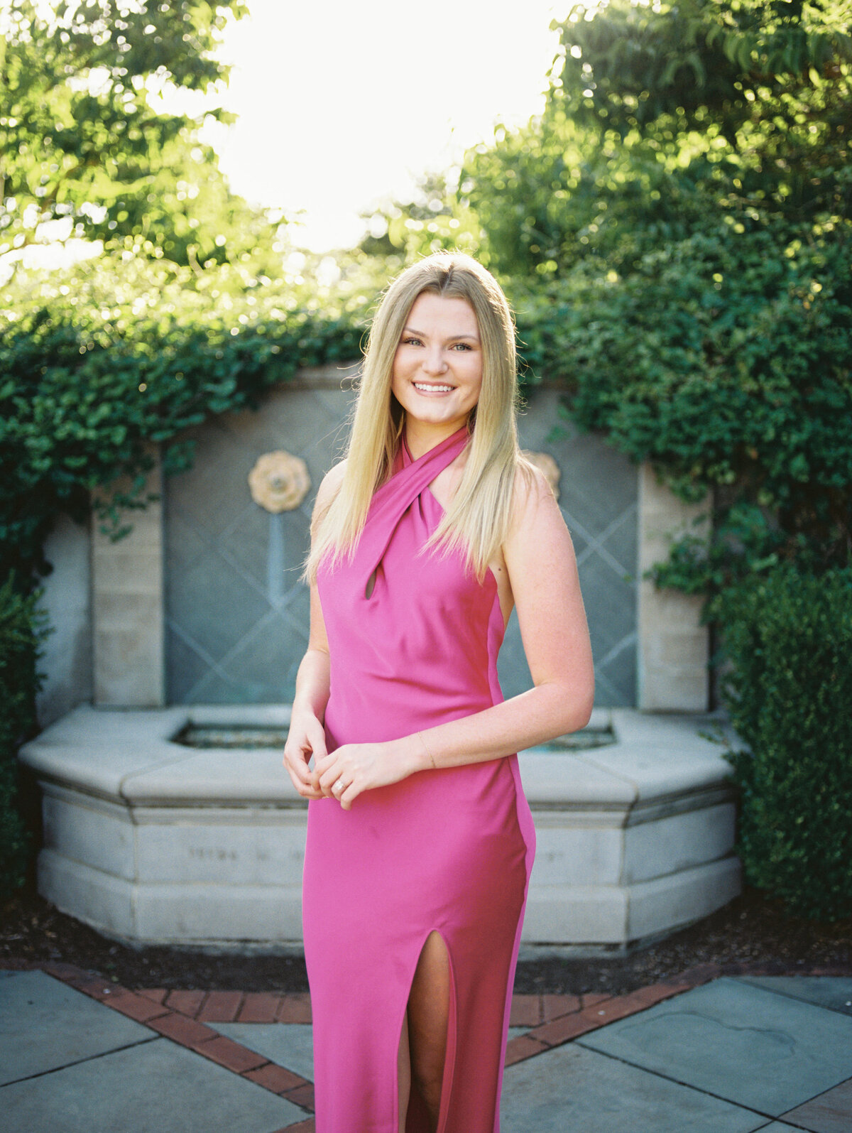 Woman in pink dress poses in front of stone fountain in Columbus park.