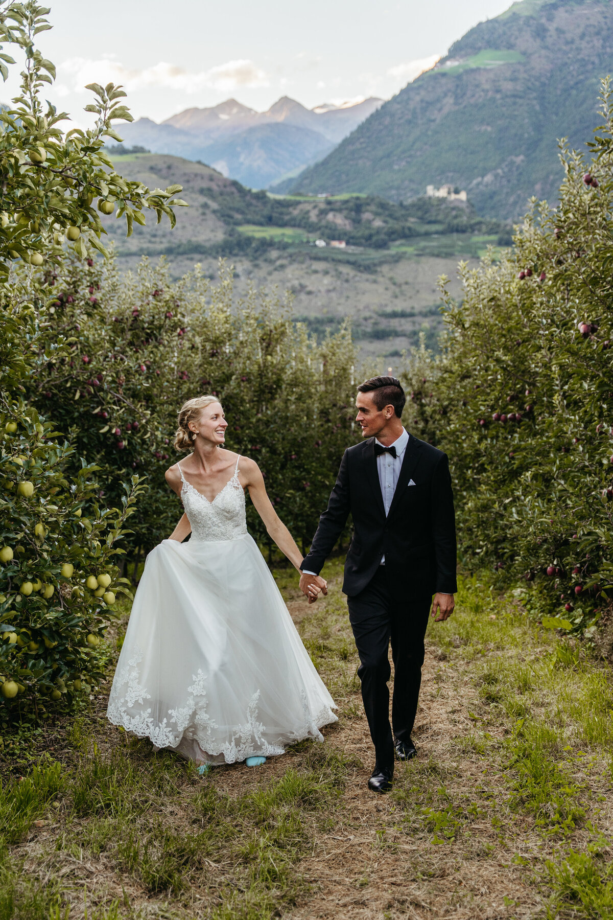 Bride and groom walking hand in hand in orchard