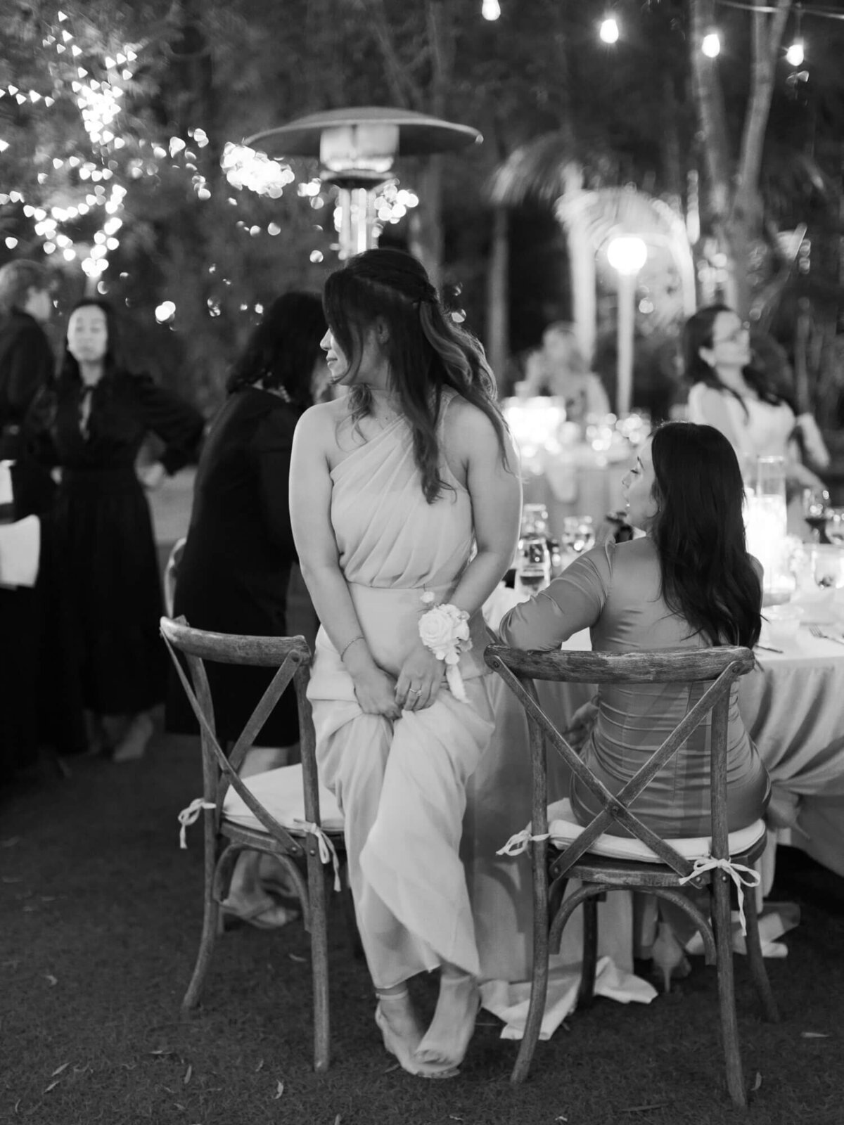 A black-and-white photo of a woman in a gown standing next to chairs at a festive, outdoor event.