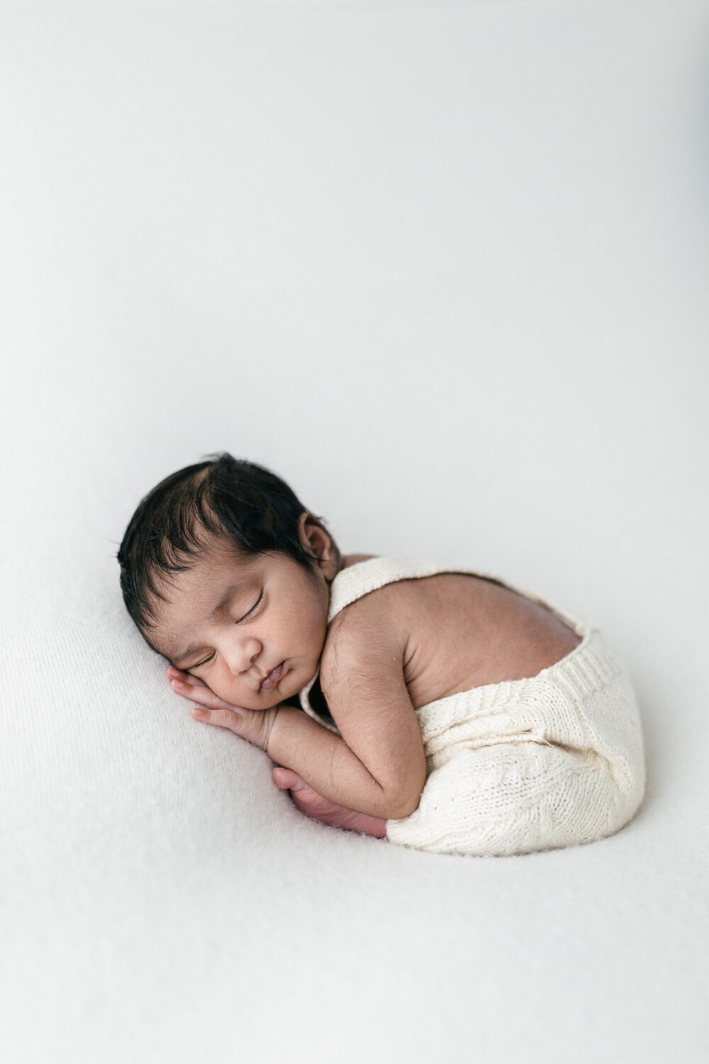 Baby in taco pose asleep against white backdrop