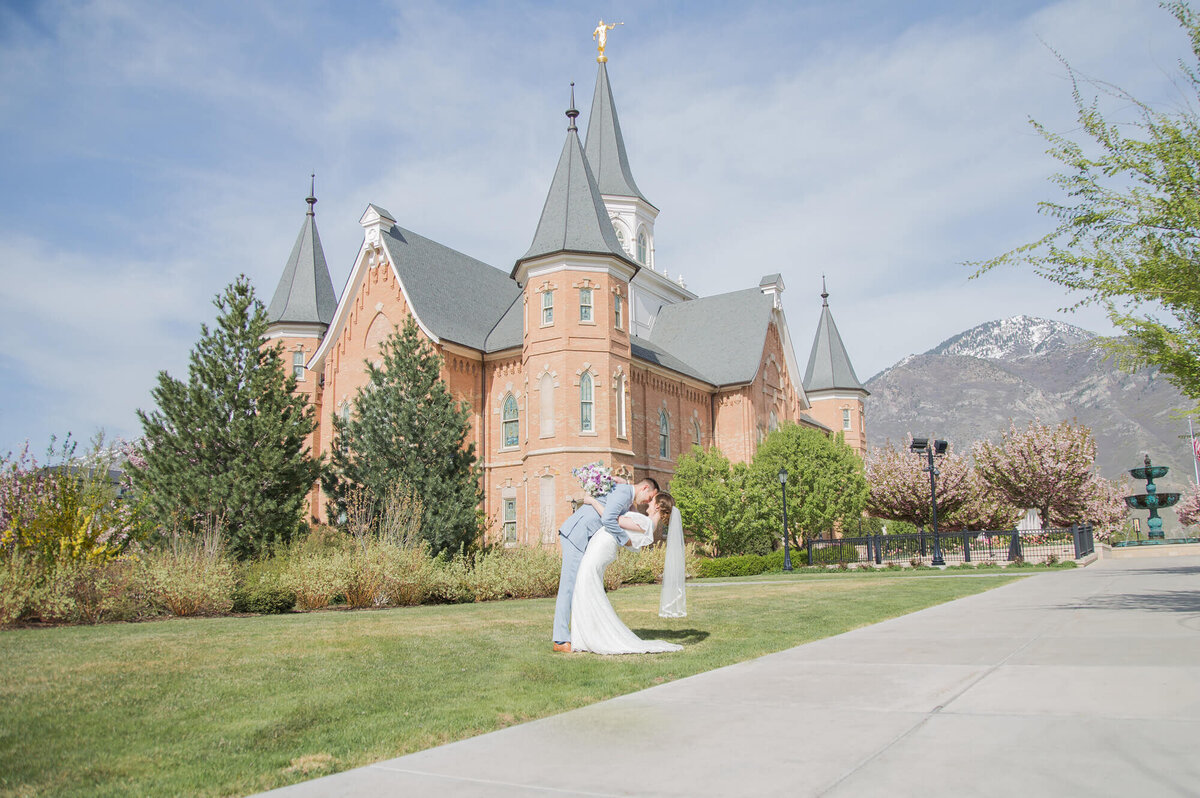 a groom dipping a bride in front of a brick lds temple