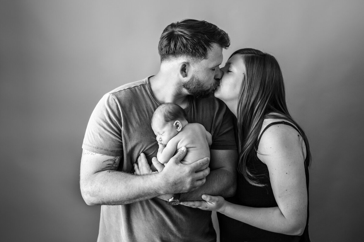 parents holding newborn girl kissing