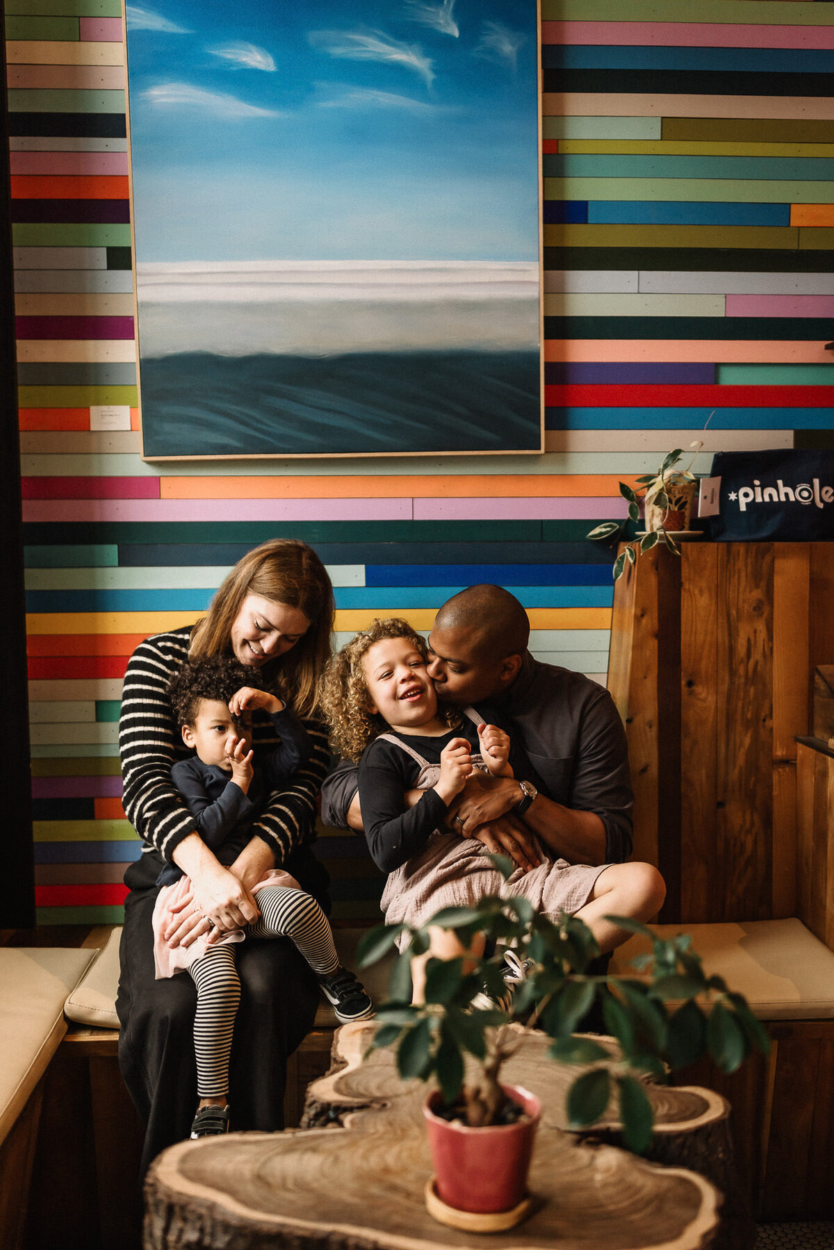 Mixed race lifestyle family photo in coffeshop with colorful stripes and cloud artwork on wall