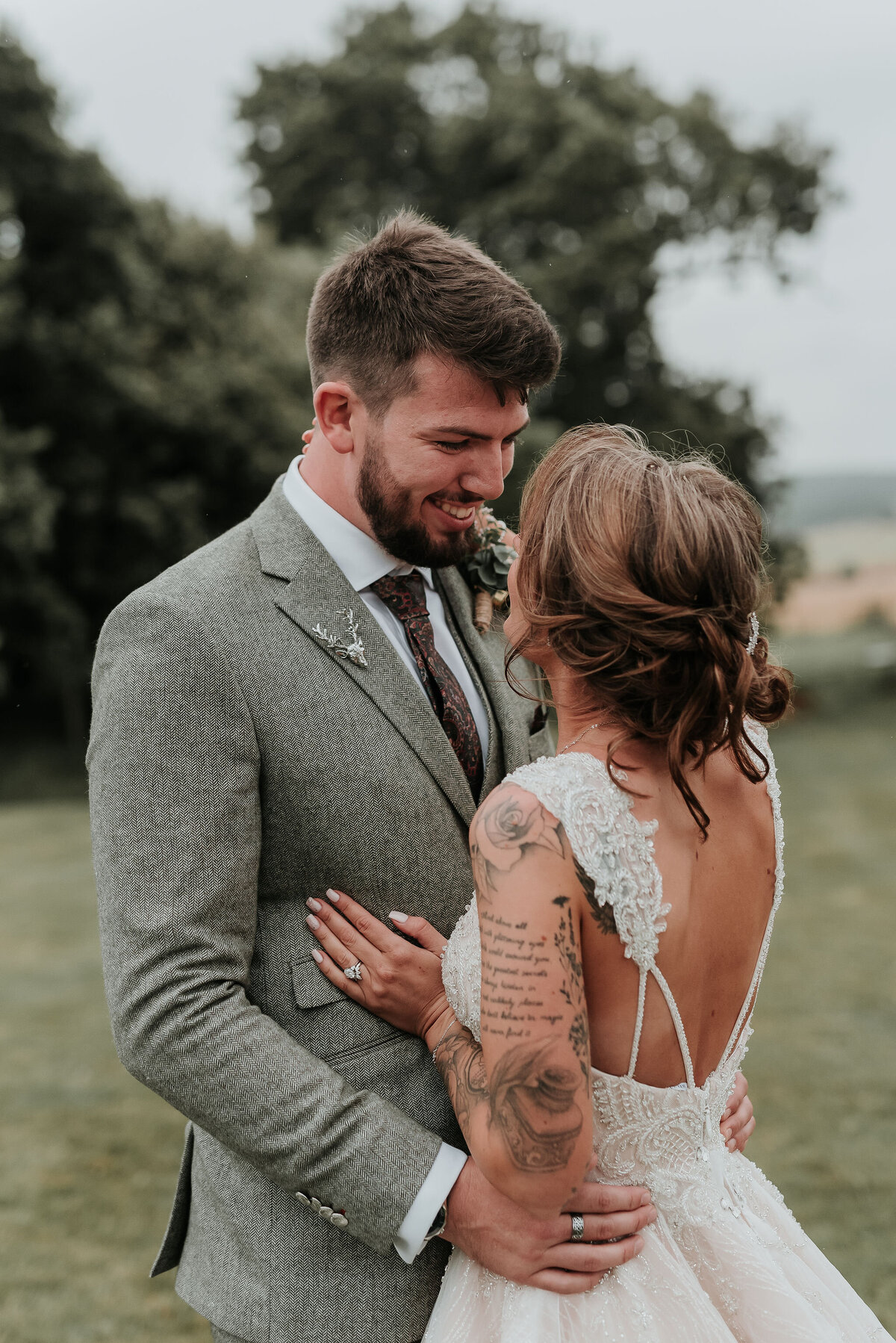 Groom in smart grey tweed suit smiles at his Bride at their barn wedding at Odo's Barn, Ashford
