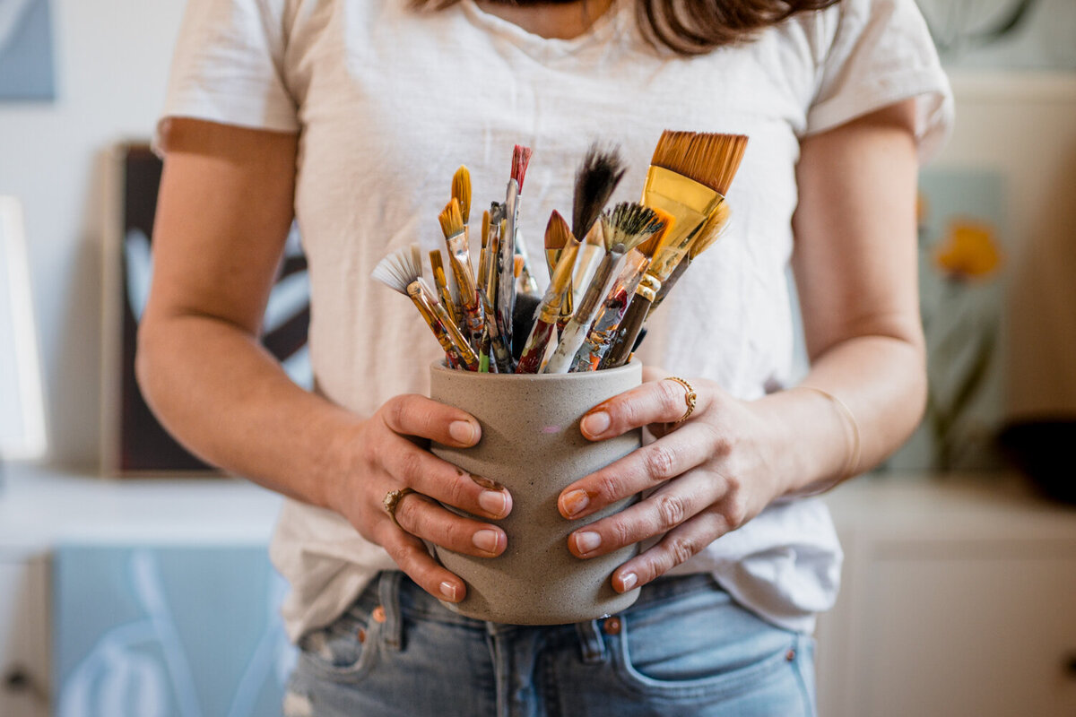 Close-up of Texas artist's hands holding paintbrushes during in-home branding session.