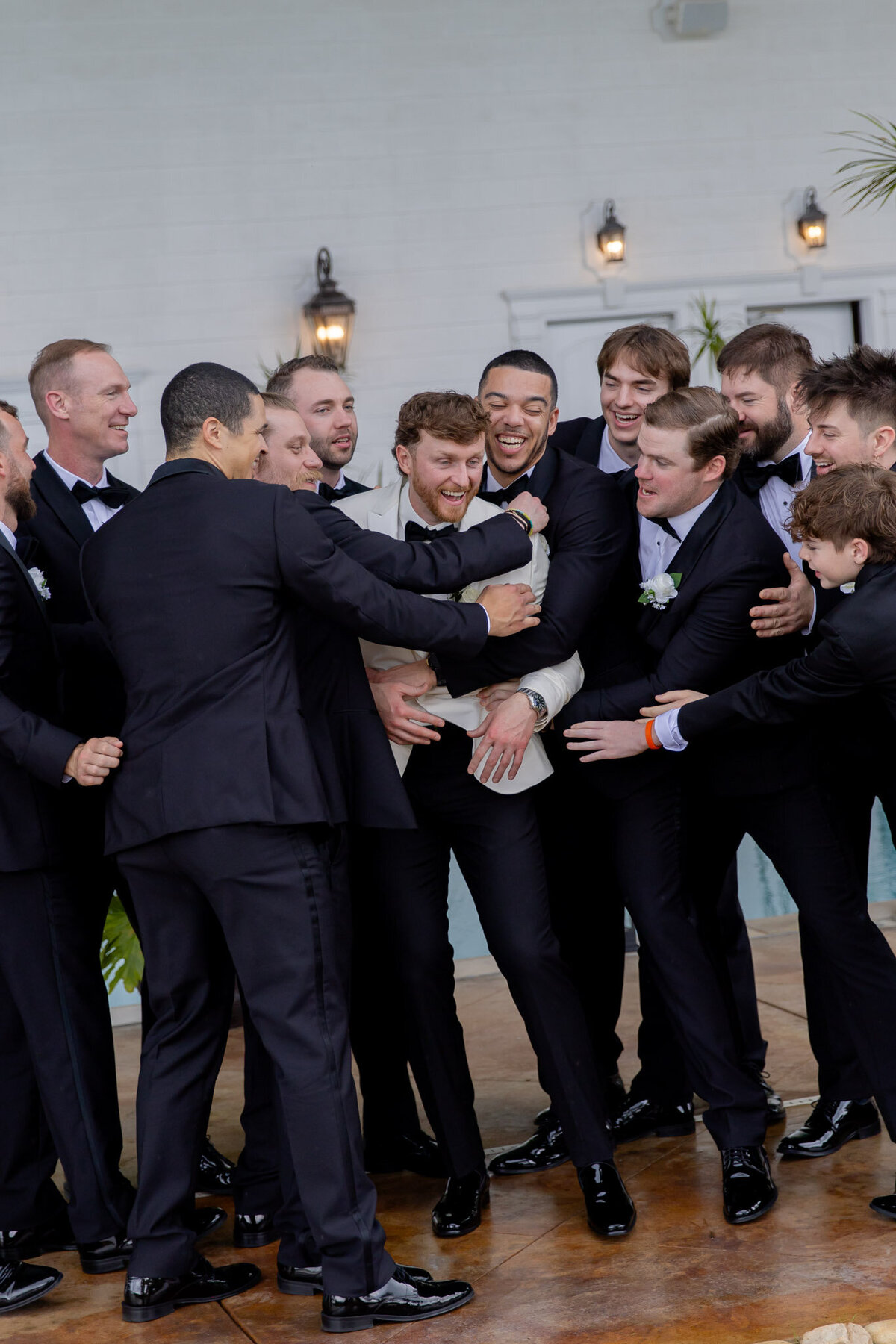 A large group of groomsmen all gather around the groom. They're all smiling and doing one big group hug.