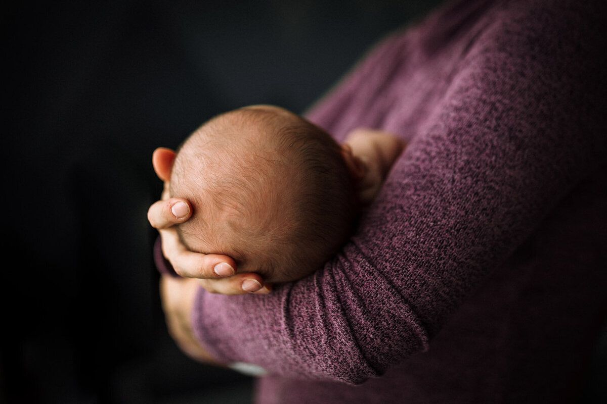 back of newborn's head in mom's arms who is wearing a purple sweater