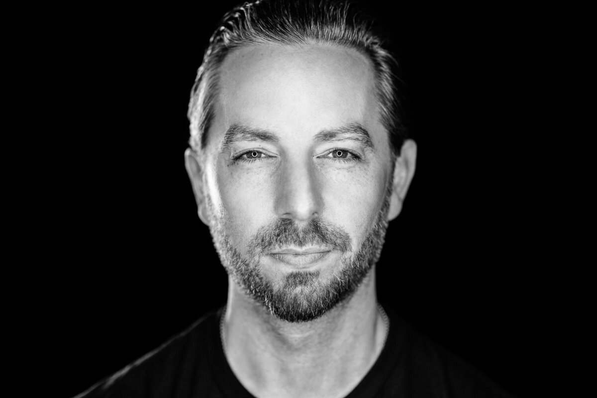 Editorial studio portrait of a man in black shirt photographed in a dramatic lighting setup.