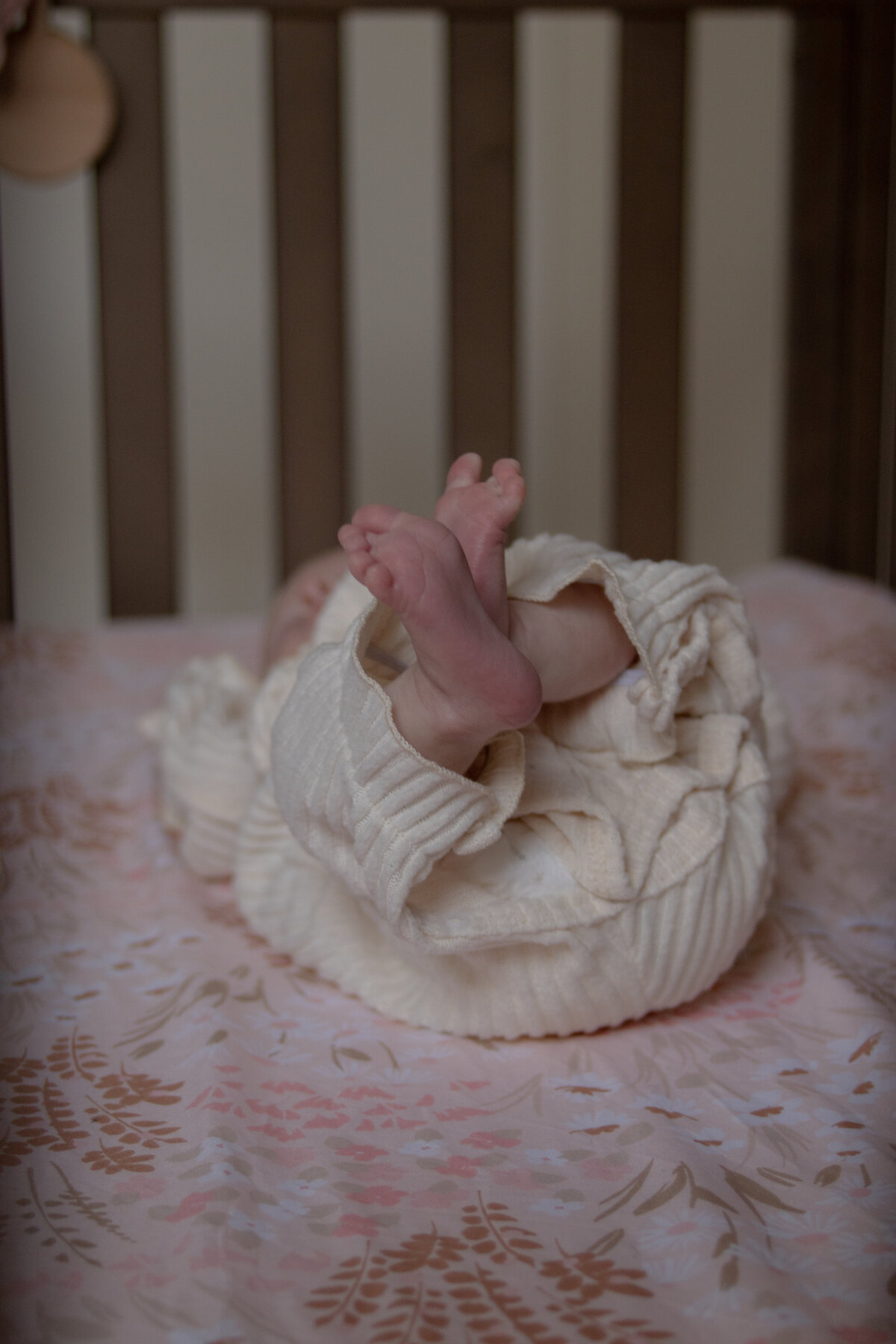 close up of newborn baby girl's feet while she lays in her crib on floral, pink sheets