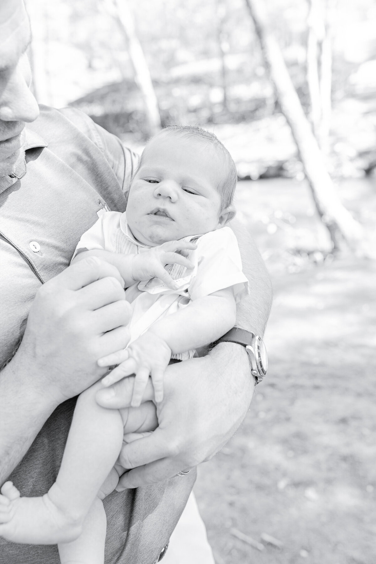 Newborn baby in father's arms – captured by a Birmingham newborn photographer. A sweet newborn gazes softly while cradled in dad’s strong hands, capturing the warmth and security of early parenthood in this natural, outdoor session.