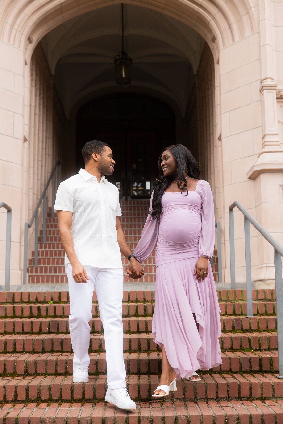 The couple strolls down a set of stairs on the University of Washington campus, sharing a joyful moment as they smile together, enjoying their time as they look forward to their future.