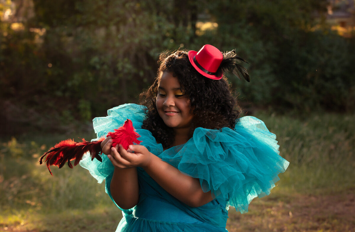 girl-holding-red-bird-in-blue-dress-with-red-tiny-hat-in-dalworthington-gardens-tx