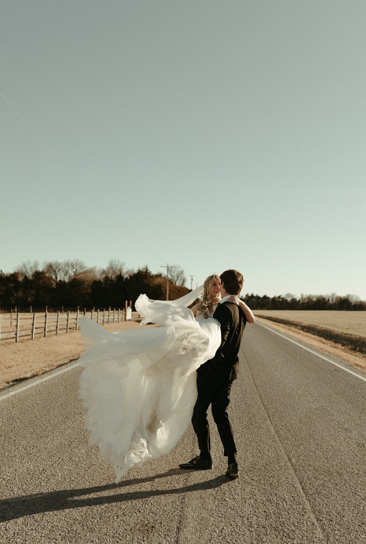 groom holding bride while spinning in street