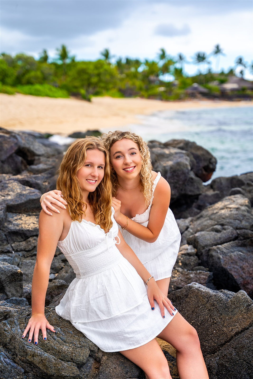 Two girls smiling and standing on lava rocks taken by big island family photographers

