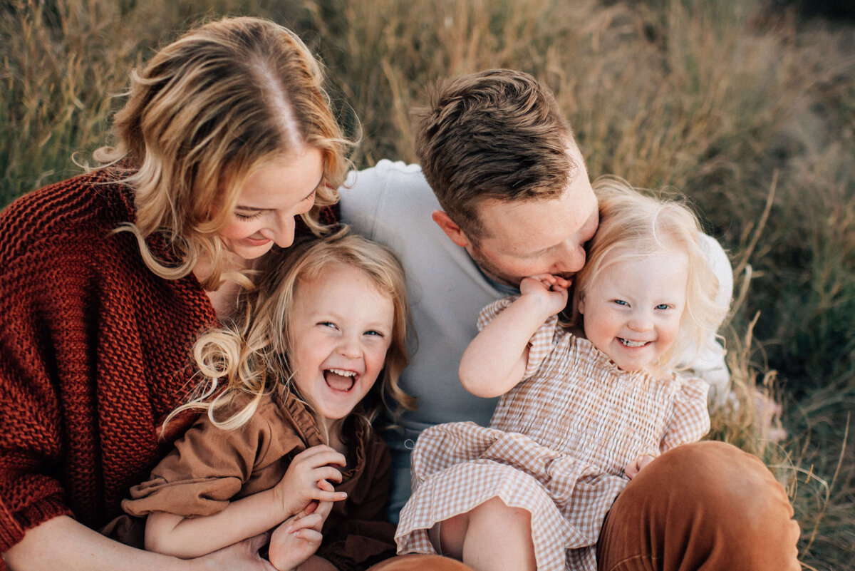 family of four with two girls snuggling in the grass