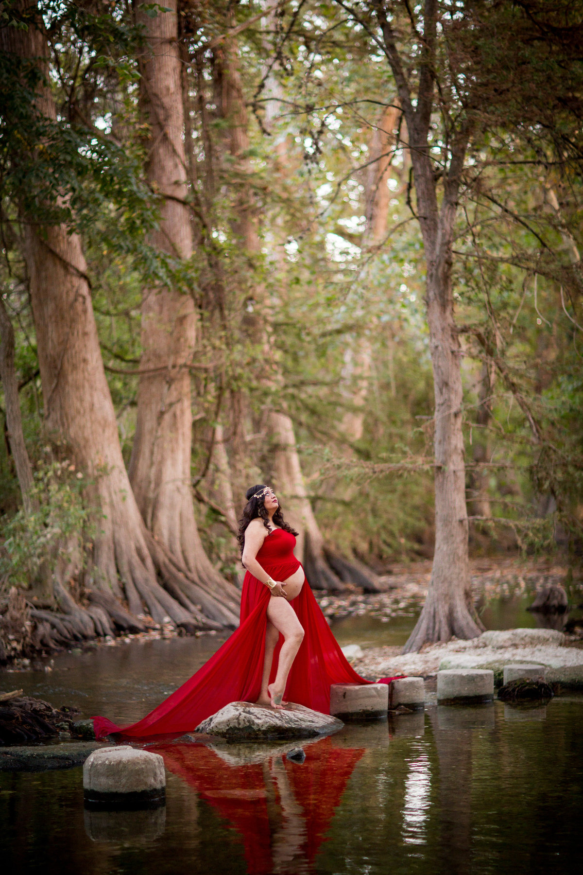 Maternity picture of pregnant woman in red dress holding baby belly and standing in a river.