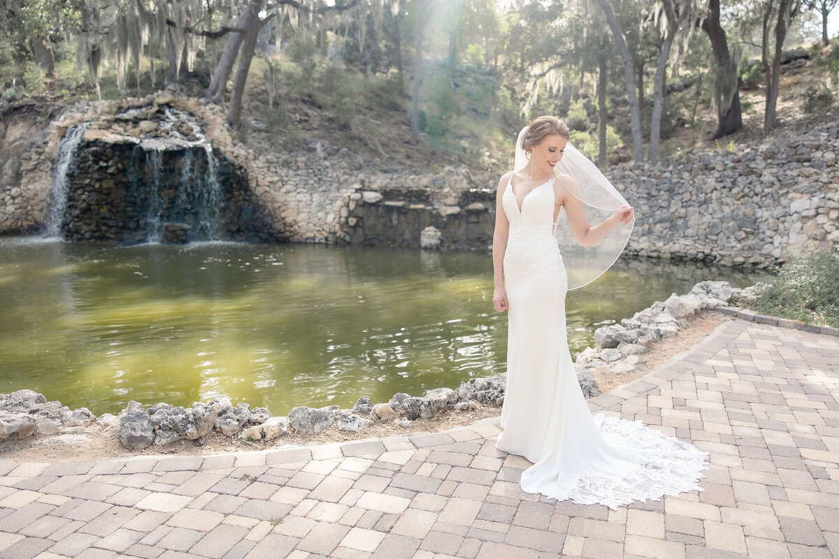 bride in v neck gown holding veil with waterfalls at Hayes Hollow at Hidden Falls in Spring Branch Texas