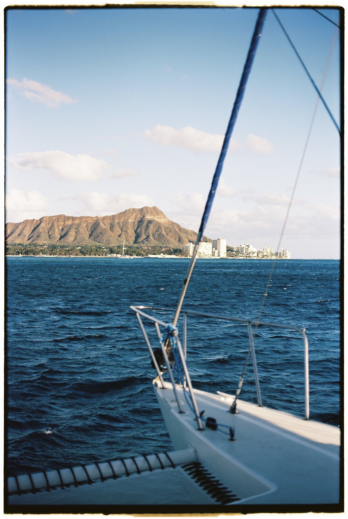 Catamaran sailing with Diamond Head in the background, captured on film by Kate Winters Photography, showcasing the natural beauty and scenic views in an authentic, documentary style.
