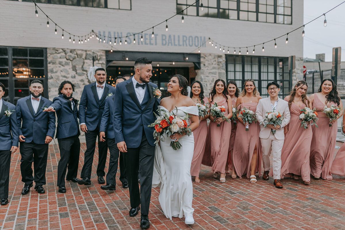 Bride and groom walking outside with entourages in the back