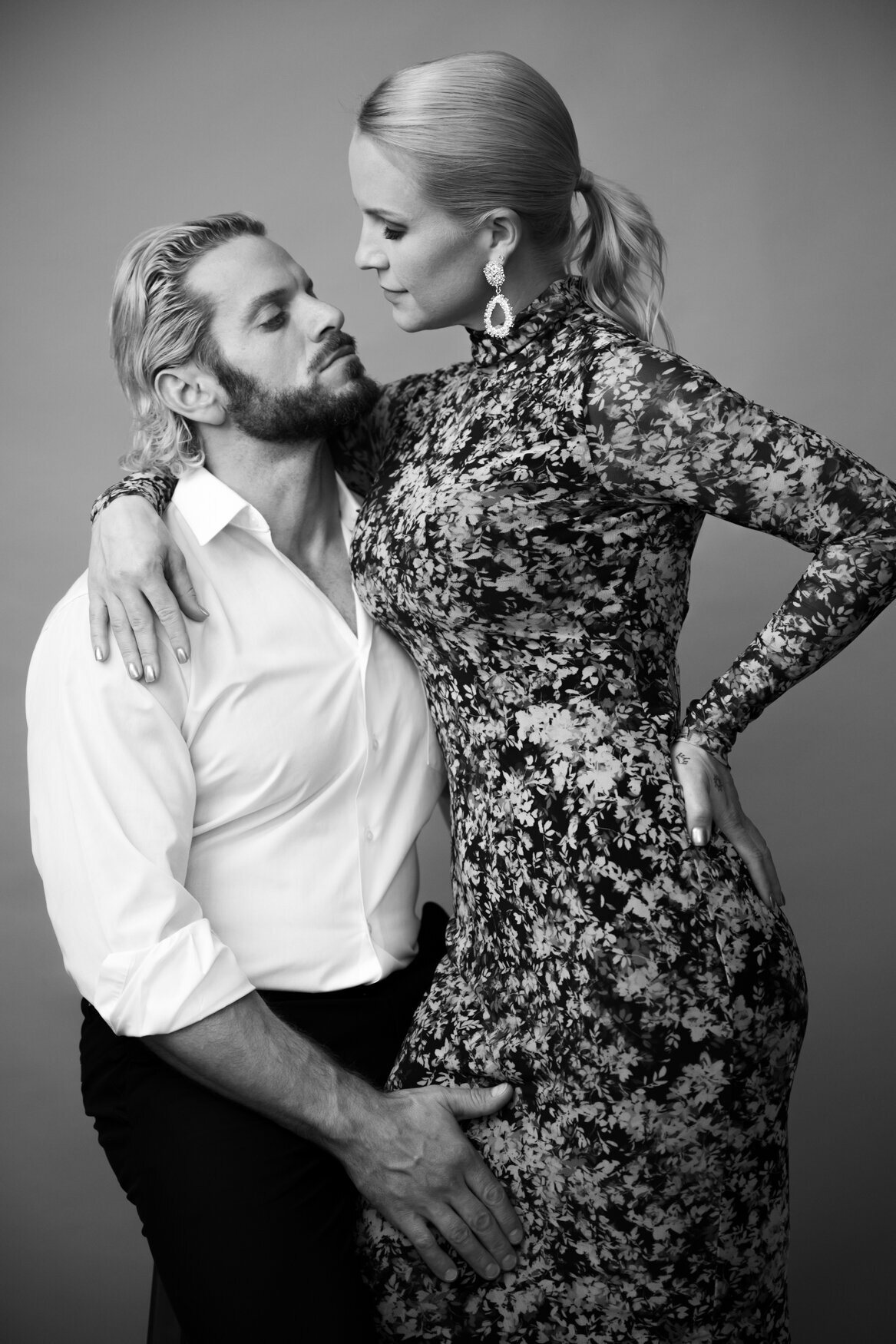 man sitting on a stool hugging a woman and touching her leg while she put her arm around him looking at his eyes