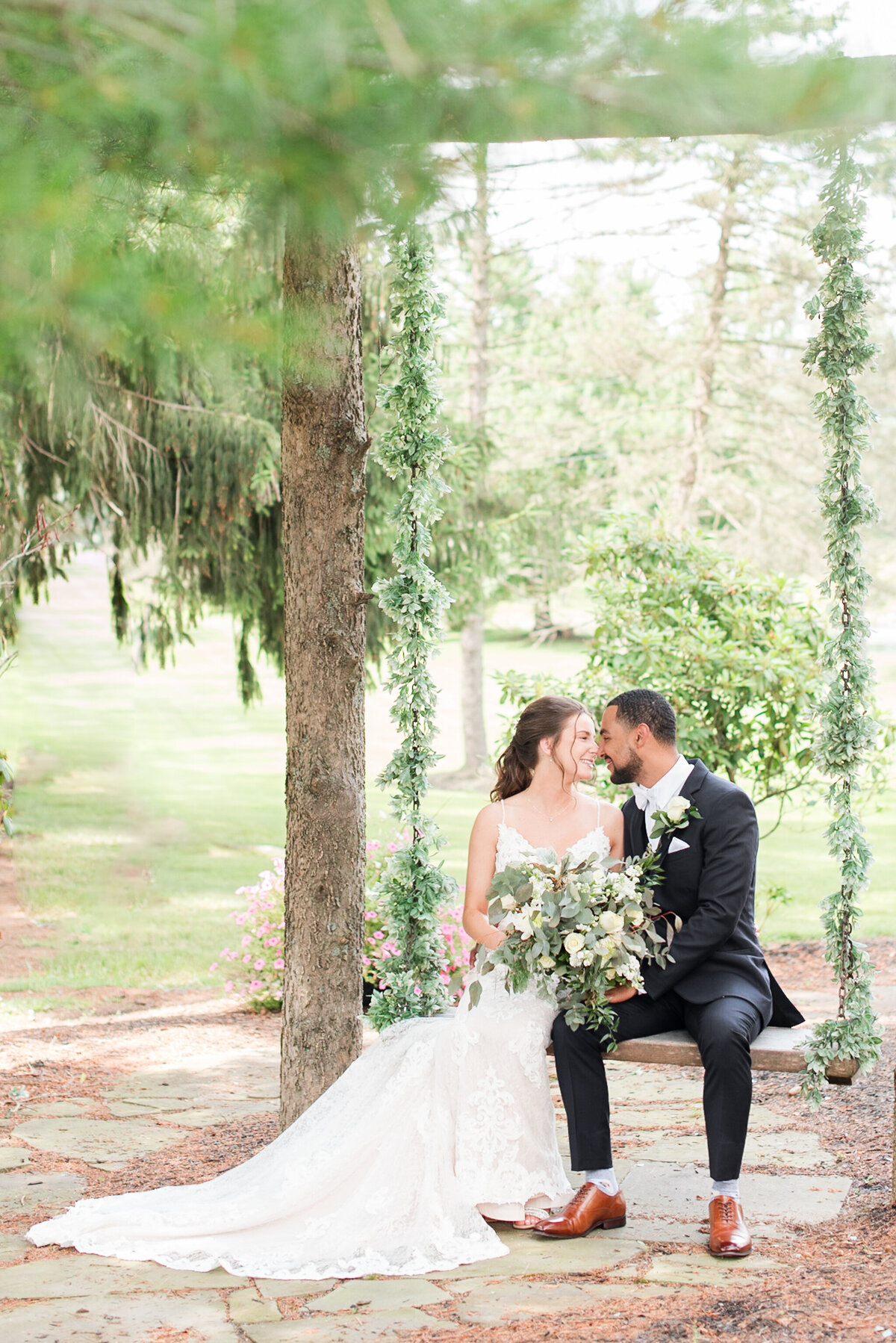 biracial couple kissing on wedding day on swing with florals adorning it