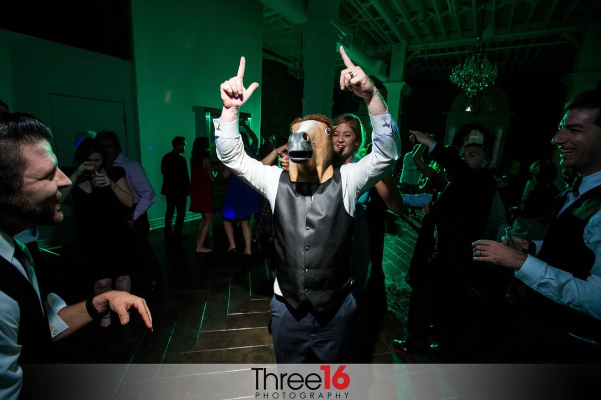 Wedding guest having a great time wearing a rubber horse head mask while on the dance floor