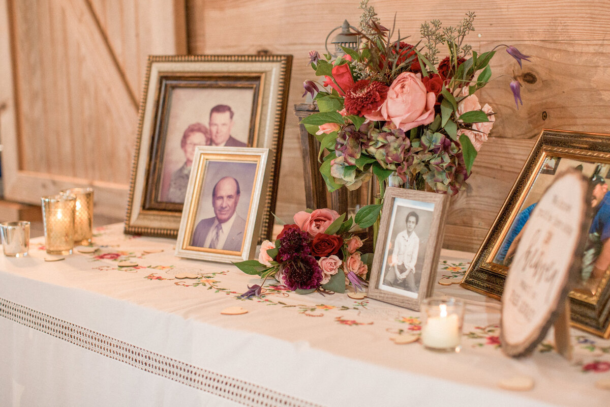 A table displaying photos of the bride and groom's departed loved ones, and decorated with florals and candles